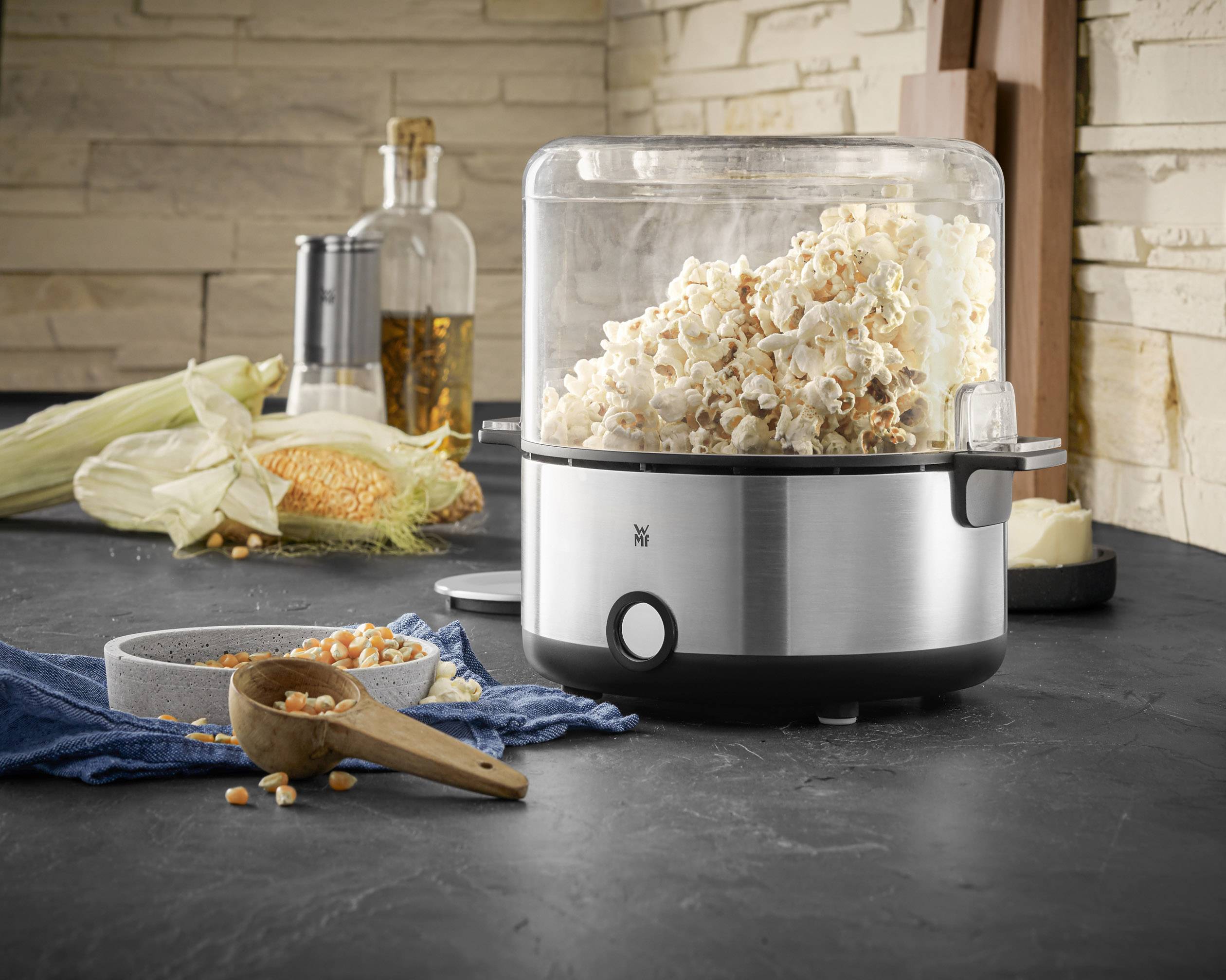 Macchina per popcorn su un piano da cucina. Popcorn fresco fuoriesce dalla macchina. Sullo sfondo, pannocchie di mais e spezie.