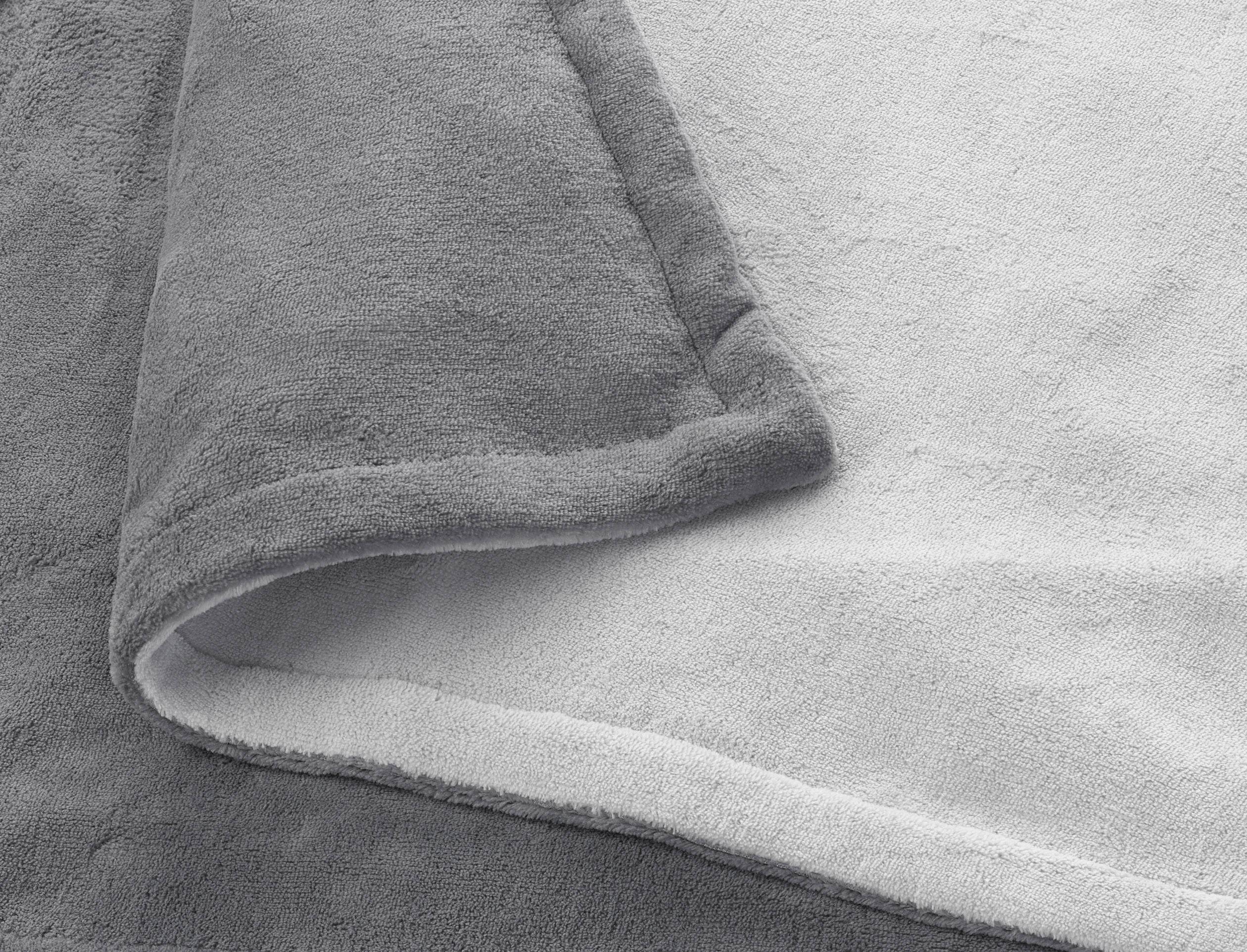Una coperta morbida e pelosa in tonalità di grigio, parzialmente ripiegata che mostra la tessitura del tessuto.