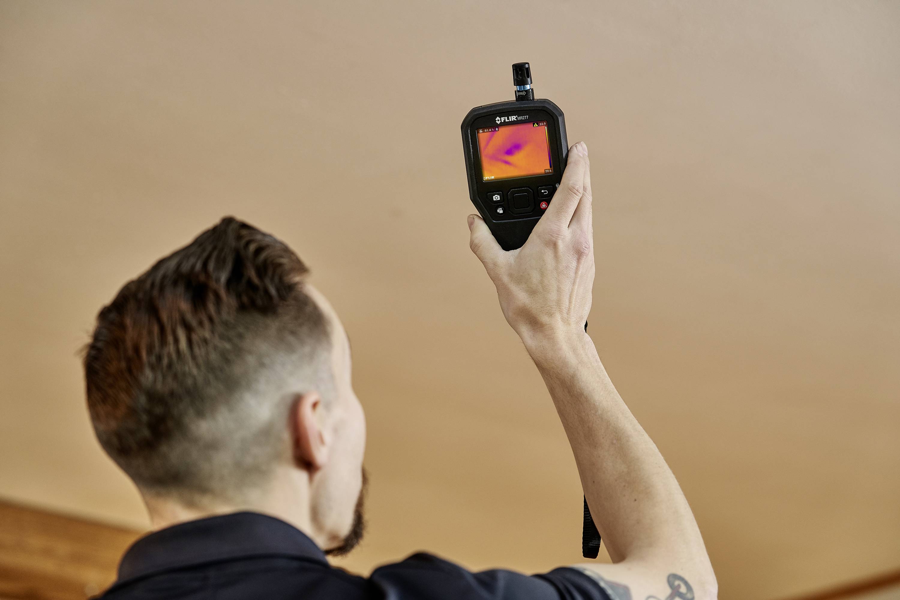 Una persona tiene una termocamera che mostra un display a colori delle temperature. La telecamera è rivolta verso l'alto.