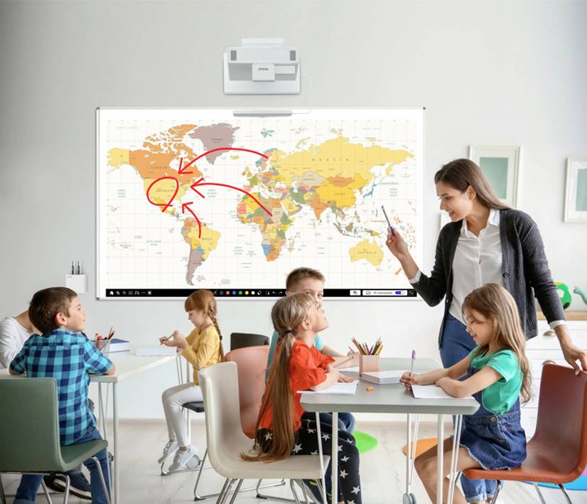Un'insegnante è in piedi davanti a una cartina geografica sulla lavagna e sta insegnando a bambini seduti ai banchi. Delle frecce indicano la direzione del Nord America.