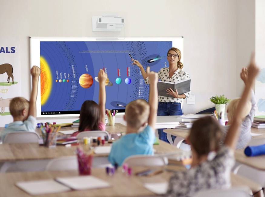 Un'insegnante spiega il sistema solare su una lavagna digitale in una classe. Gli studenti sono seduti e alzano la mano.