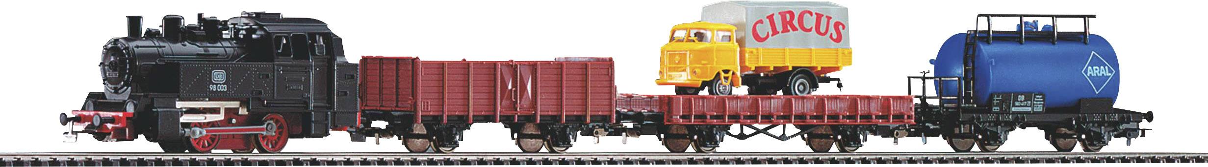 Trenino su un binario. Il treno è composto da una locomotiva nera e diversi vagoni merci, tra cui un carro cisterna e un vagone aperto con modelli di camion.