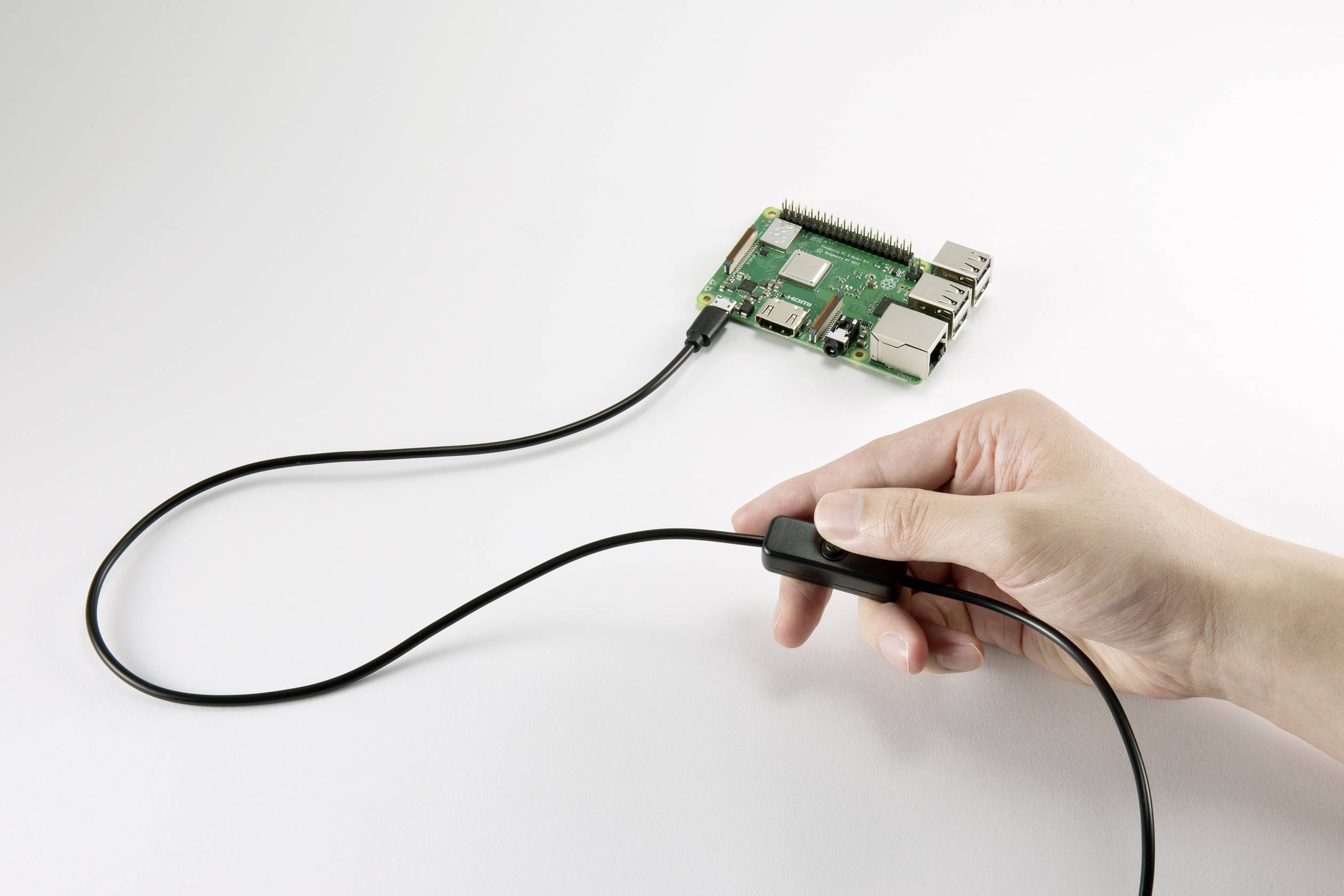Una mano tiene la spina di un cavo collegato a un microcomputer. Il microcomputer è poggiato su una superficie bianca.