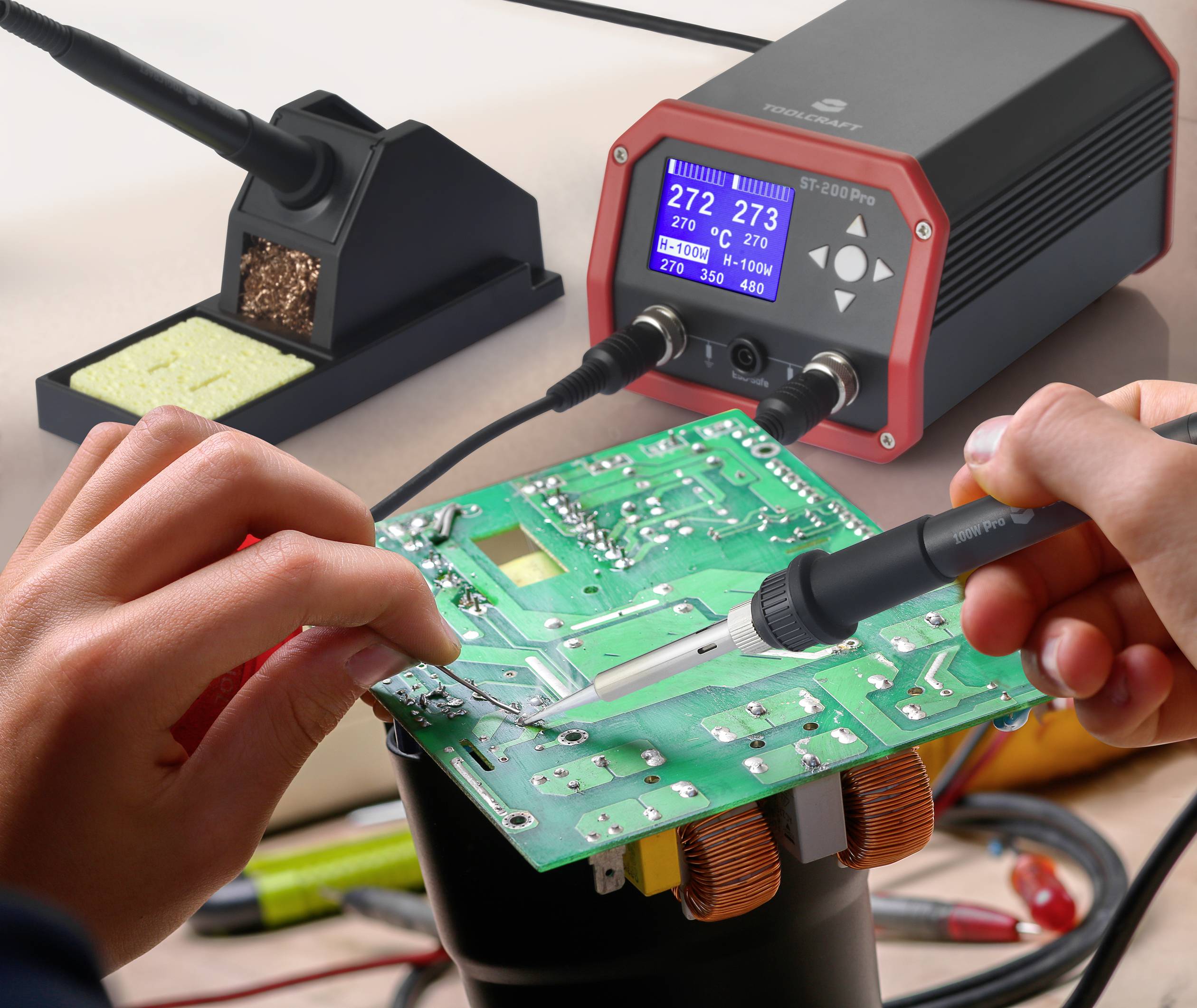 Due mani tengono un saldatore e una scheda a circuito stampato; sullo sfondo un supporto per saldatore e un indicatore di temperatura a 272°C e 273°C.