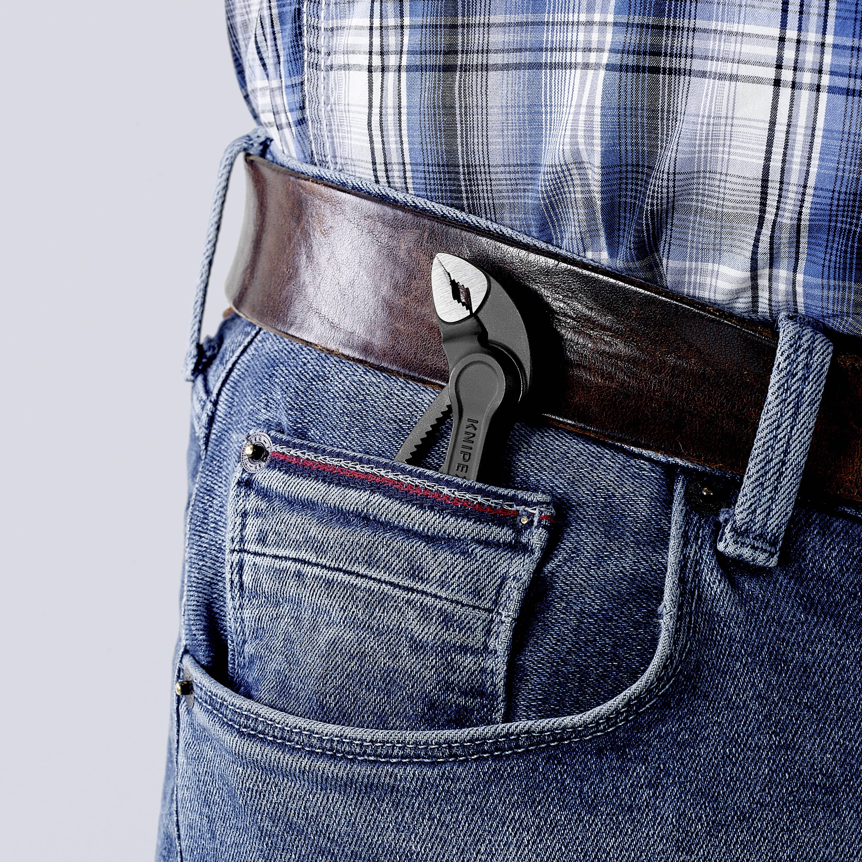 Persona con jeans blu infila una piccola chiave inglese nella tasca posteriore dei pantaloni.