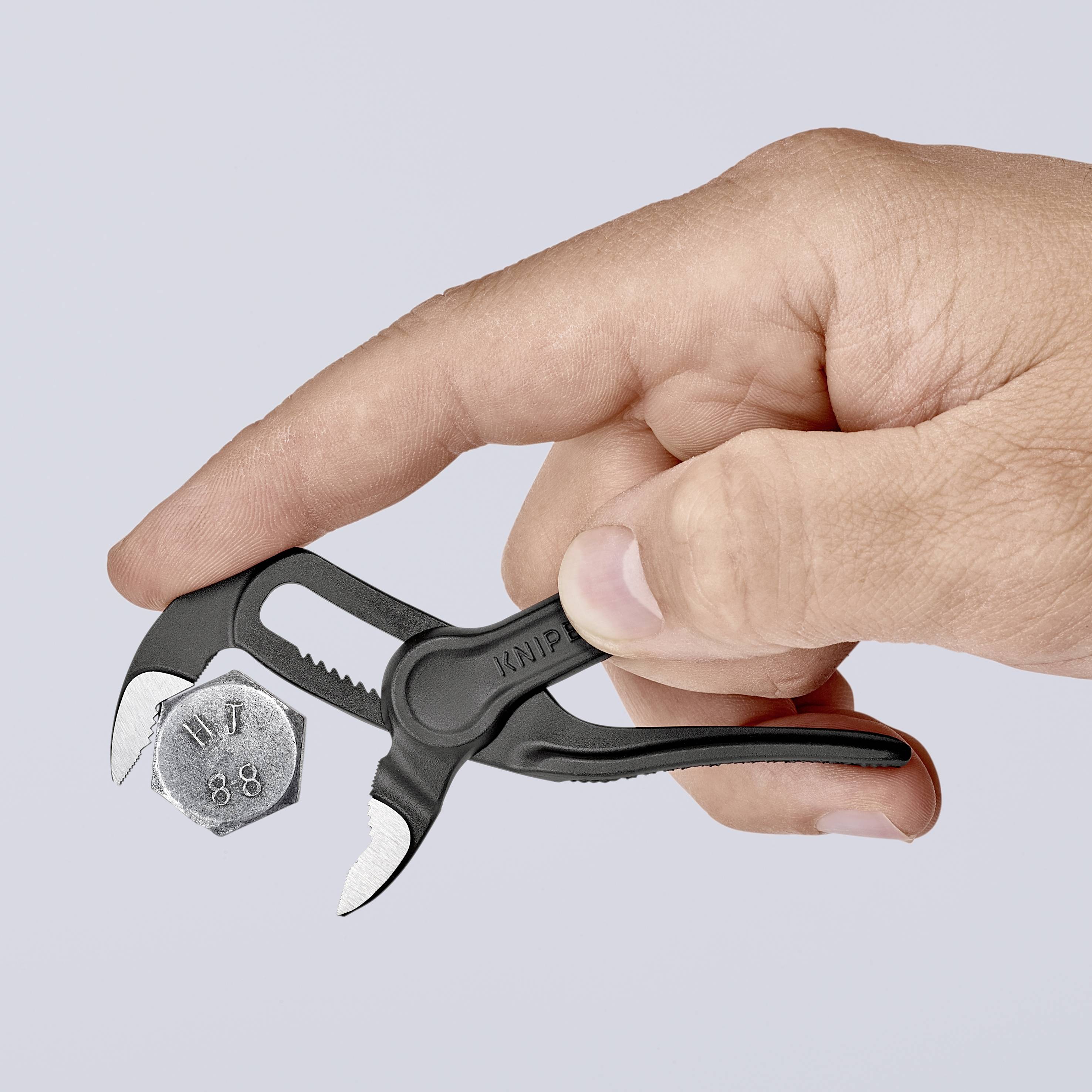 Una mano tiene una pinza che trattiene la testa di una vite. Sullo sfondo, discreto, l'attenzione è incentrata sull'operazione di lavoro.