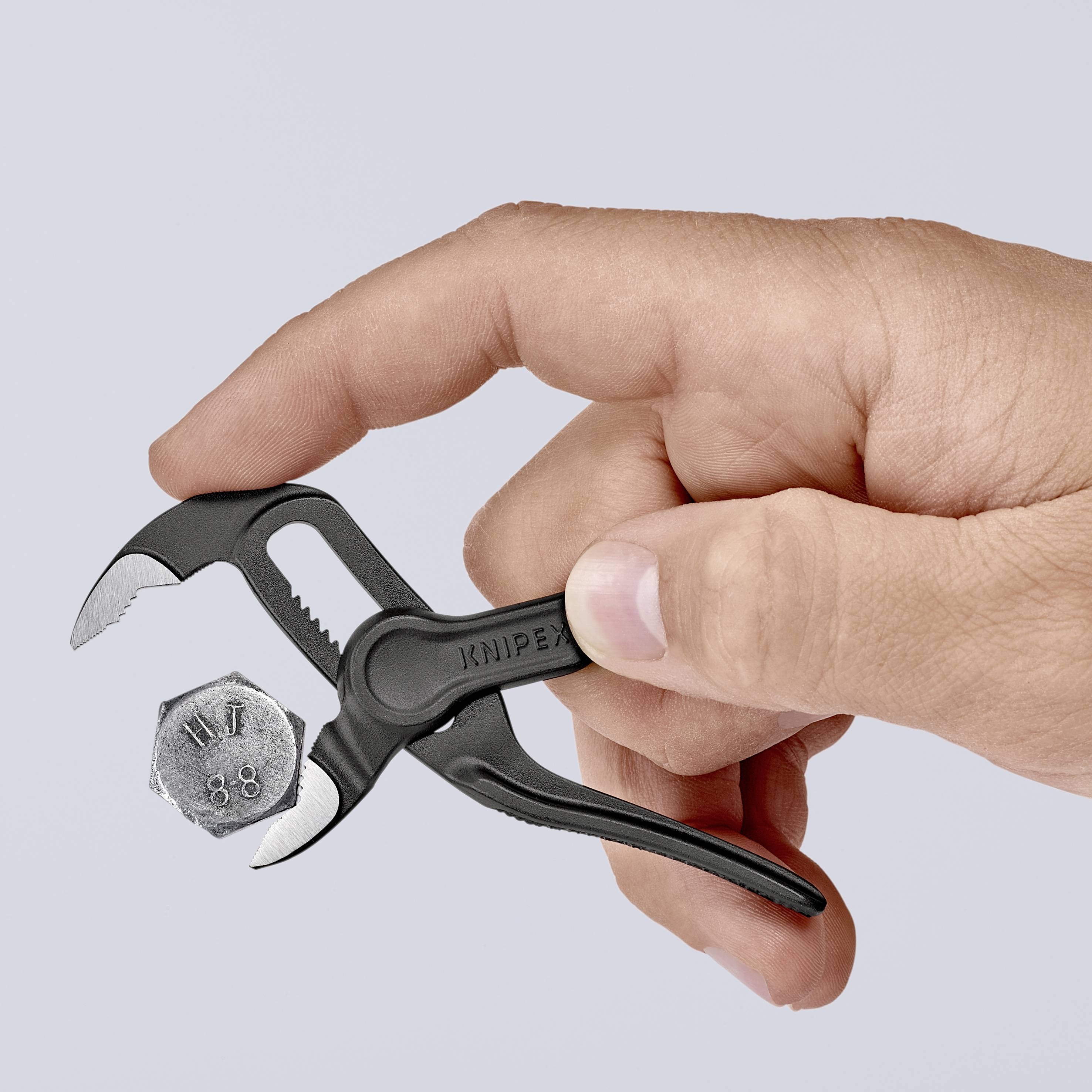 Una mano tiene una piccola pinza nera e afferra un dado esagonale. La pinza è progettata in modo funzionale e compatto.