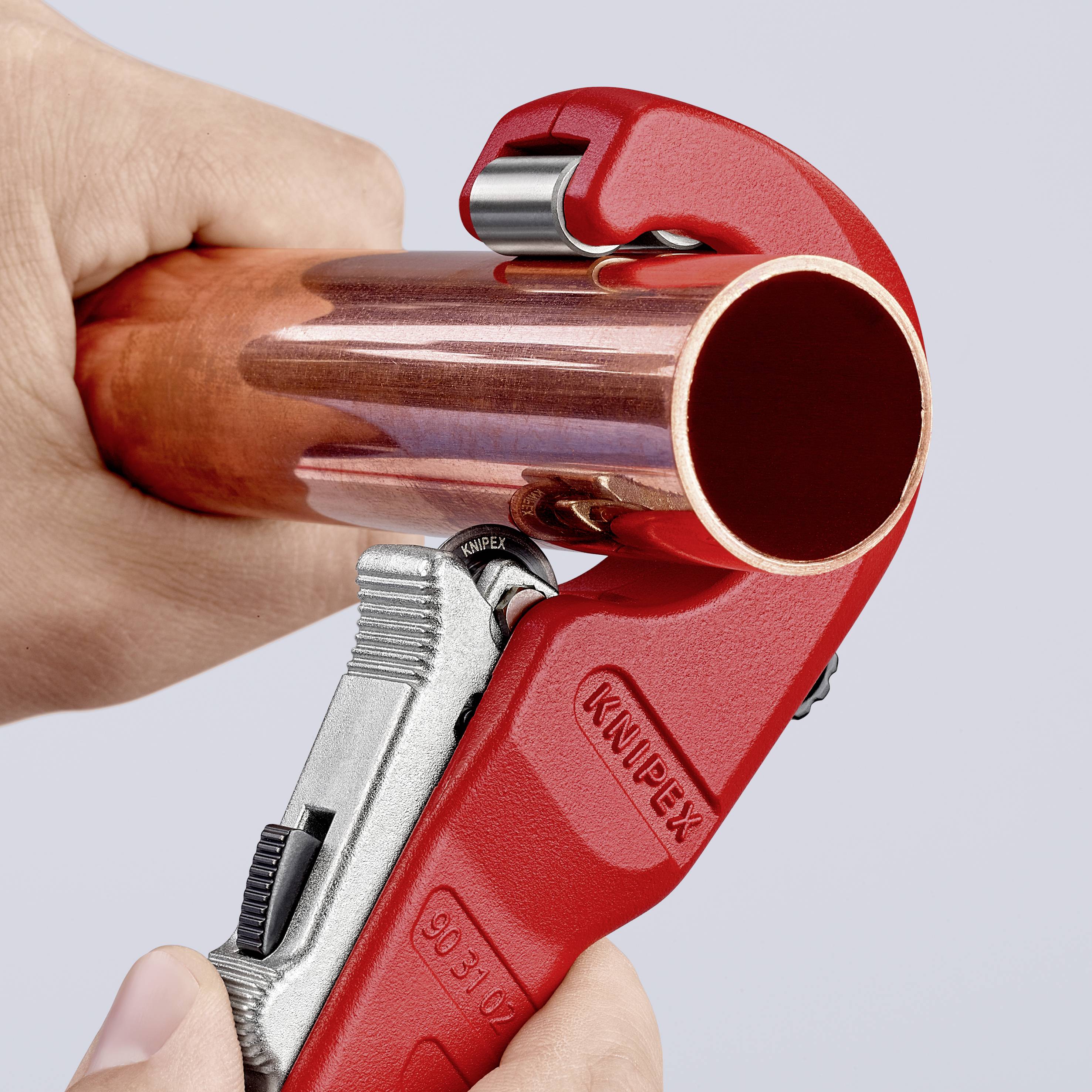 Una mano taglia un tubo di rame con un tagliatubi rosso.