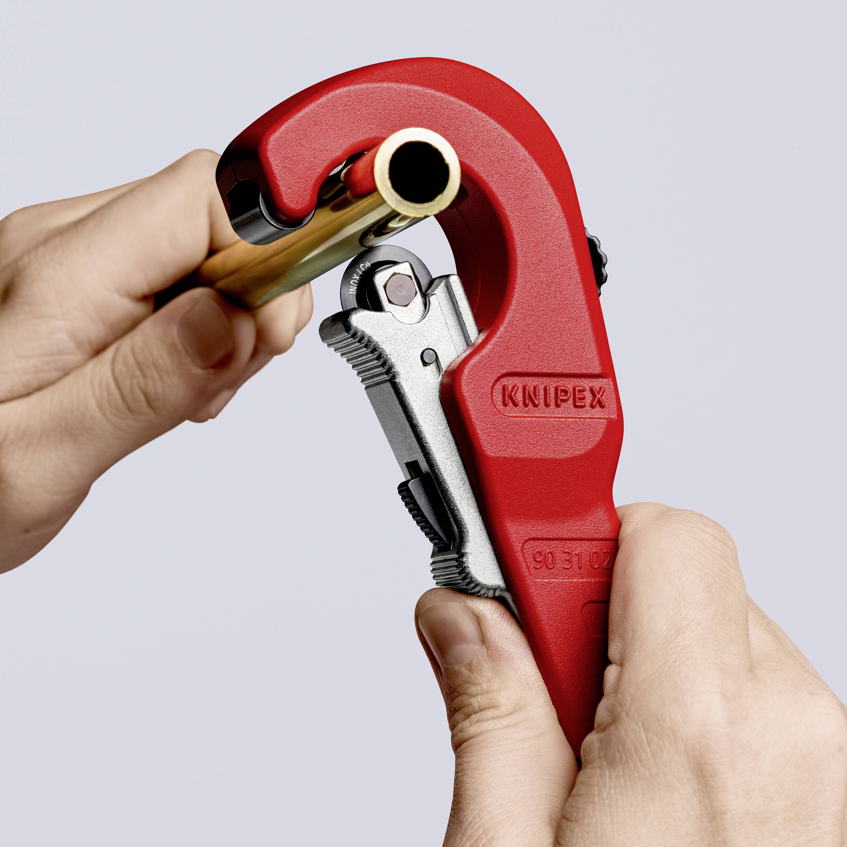 Una mano utilizza un utensile rosso per tagliare tubi, tagliando un tubo. Sullo strumento è visibile il marchio "Knipex".