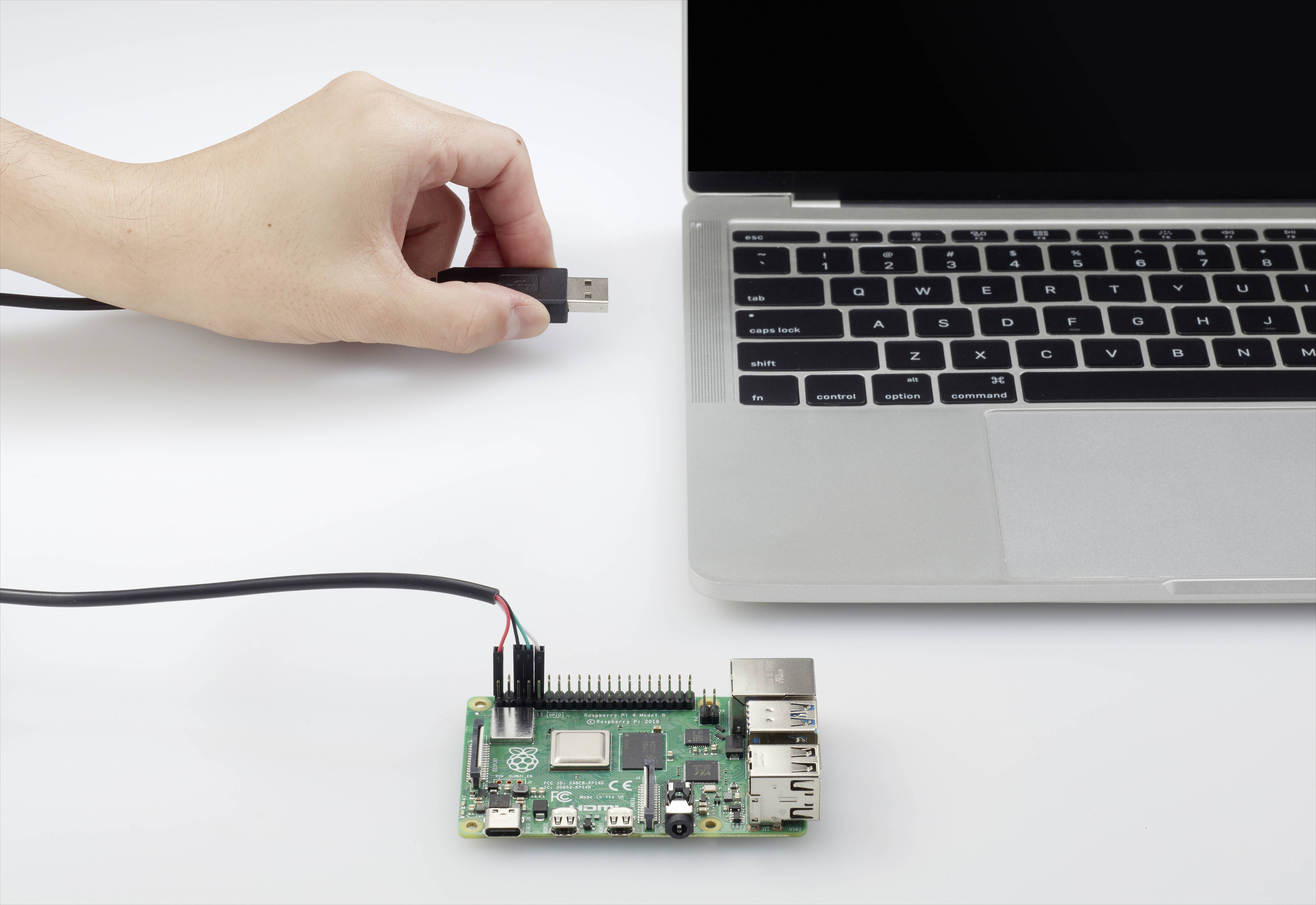 Una mano inserisce una chiavetta USB in un laptop, accanto al quale si trova un Raspberry Pi collegato con un cavo.