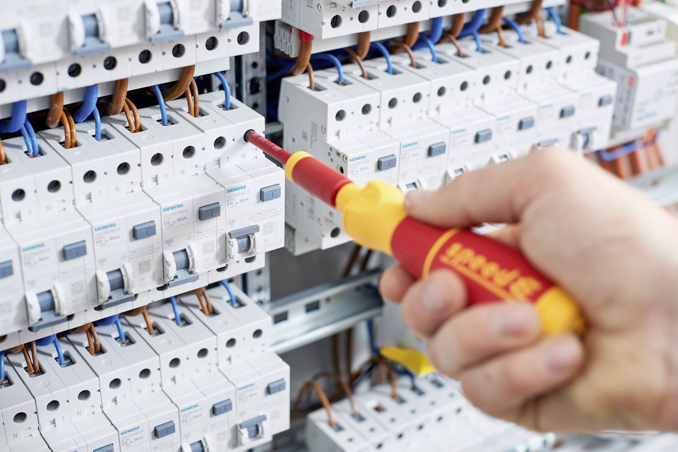 Una mano sta lavorando con un cacciavite isolato su un quadro elettrico per controllare o regolare i cavi elettrici.