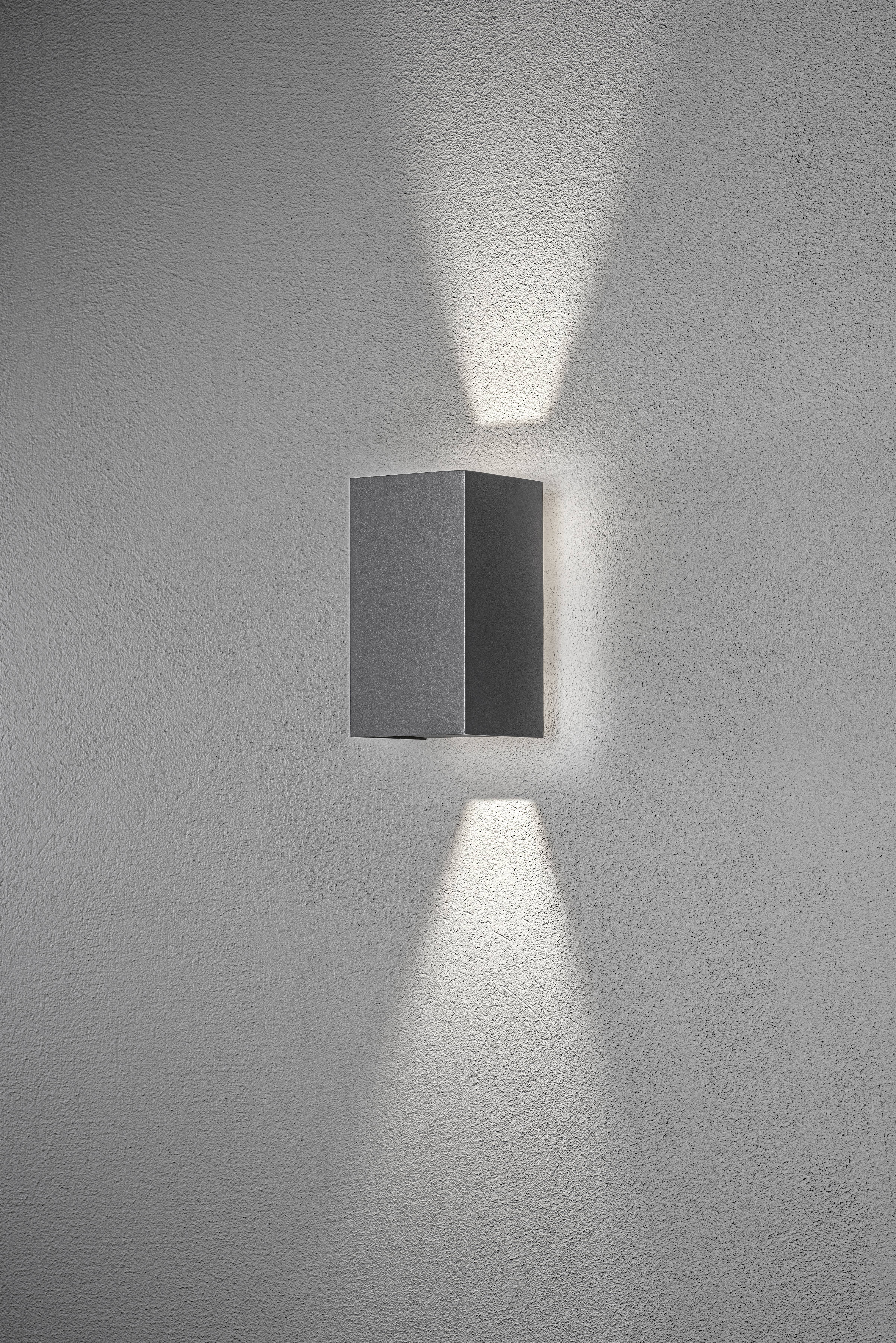 Una moderna applique nera, montata su una parete grigia, irradia la luce verso l'alto e verso il basso, creando un elegante motivo.