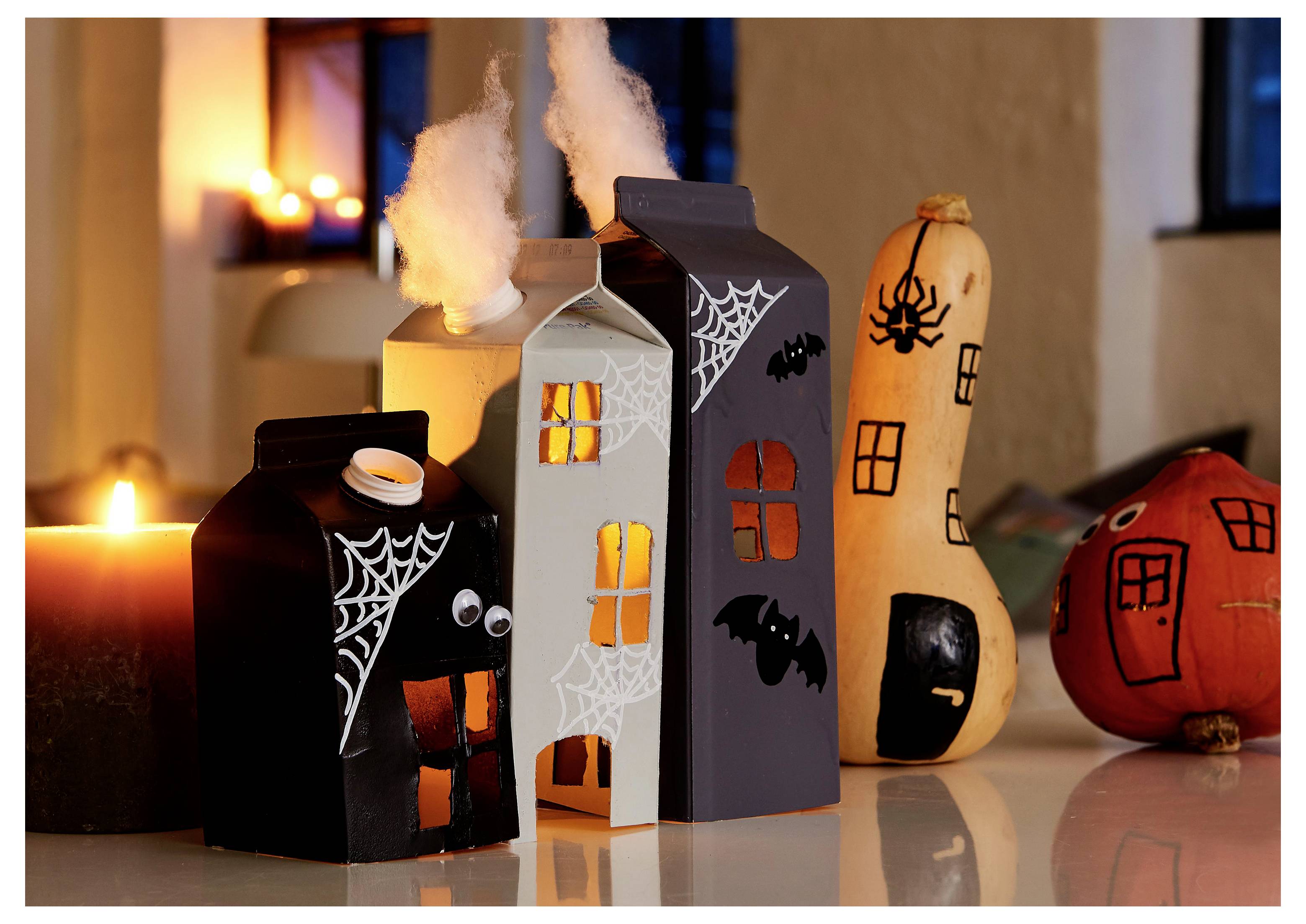 Case in miniatura a tema Halloween e zucche con decorazioni di ragnatele, pipistrelli e ragni illuminati da candele, creando un'atmosfera inquietante.