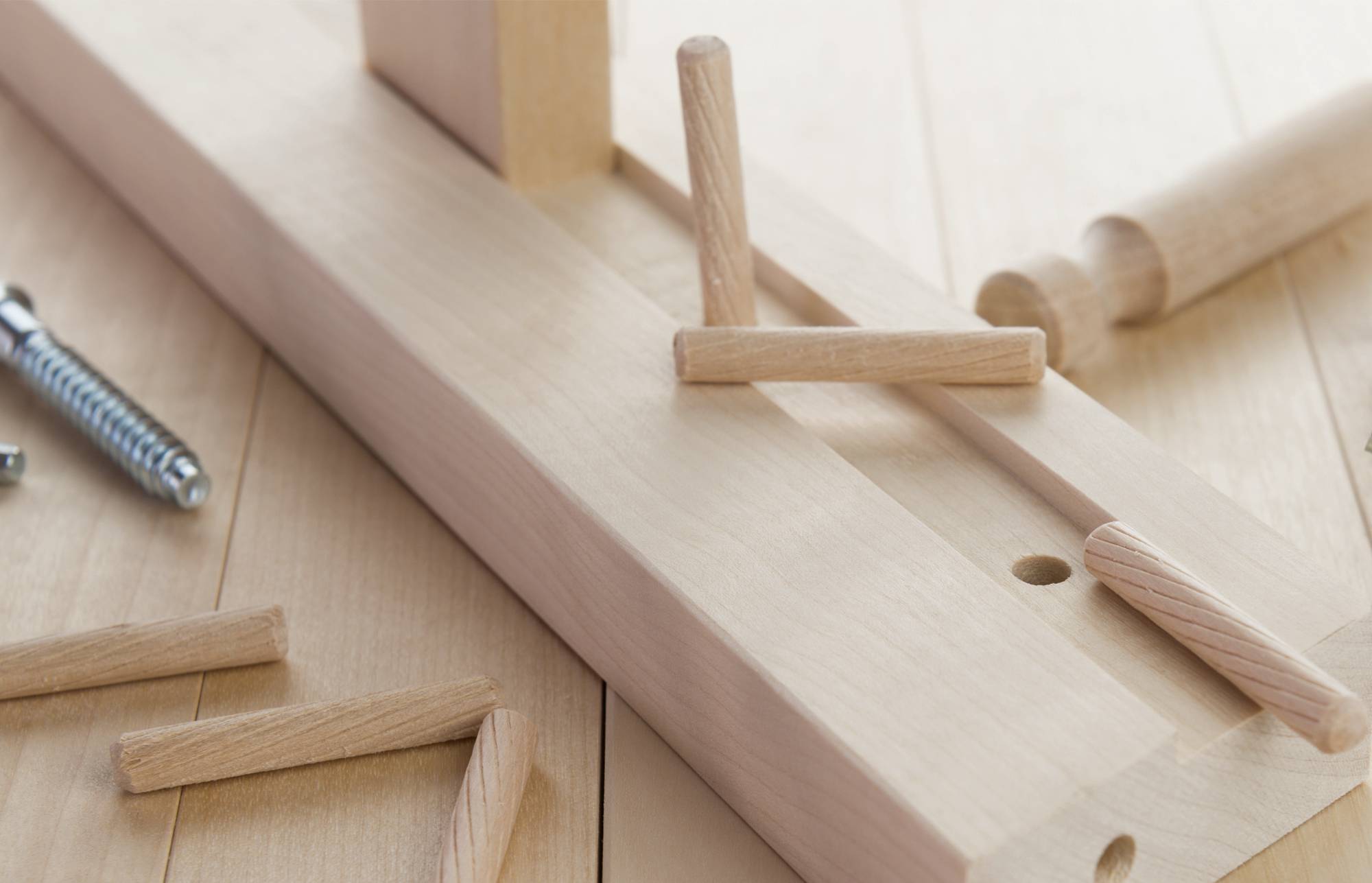 Primo piano di falegnameria di una dima in legno con pioli in legno e una morsa a molla su un banco da lavoro in legno chiaro.