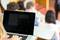 Studente in aula magna con laptop; lo schermo mostra contenuti sfocati. Altri studenti seduti sullo sfondo.