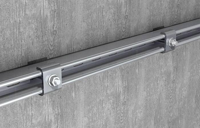 Un tubo metallico grigio, fissato orizzontalmente a una parete in cemento, è sostenuto da due grandi viti.