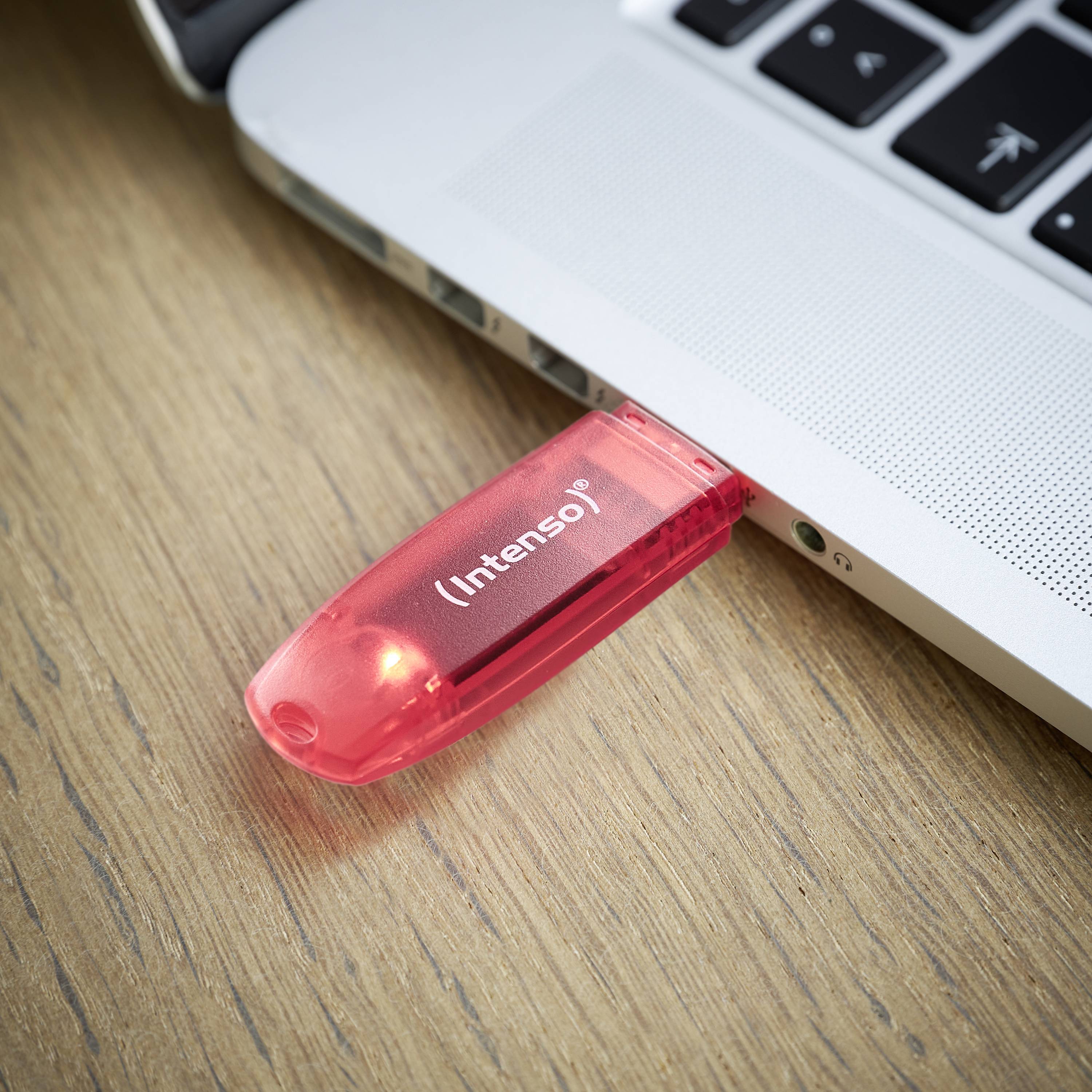 Una chiavetta USB rossa con la scritta 'Intenso' è inserita in un laptop che si trova su un tavolo di legno. La chiavetta emette una luce rossa.