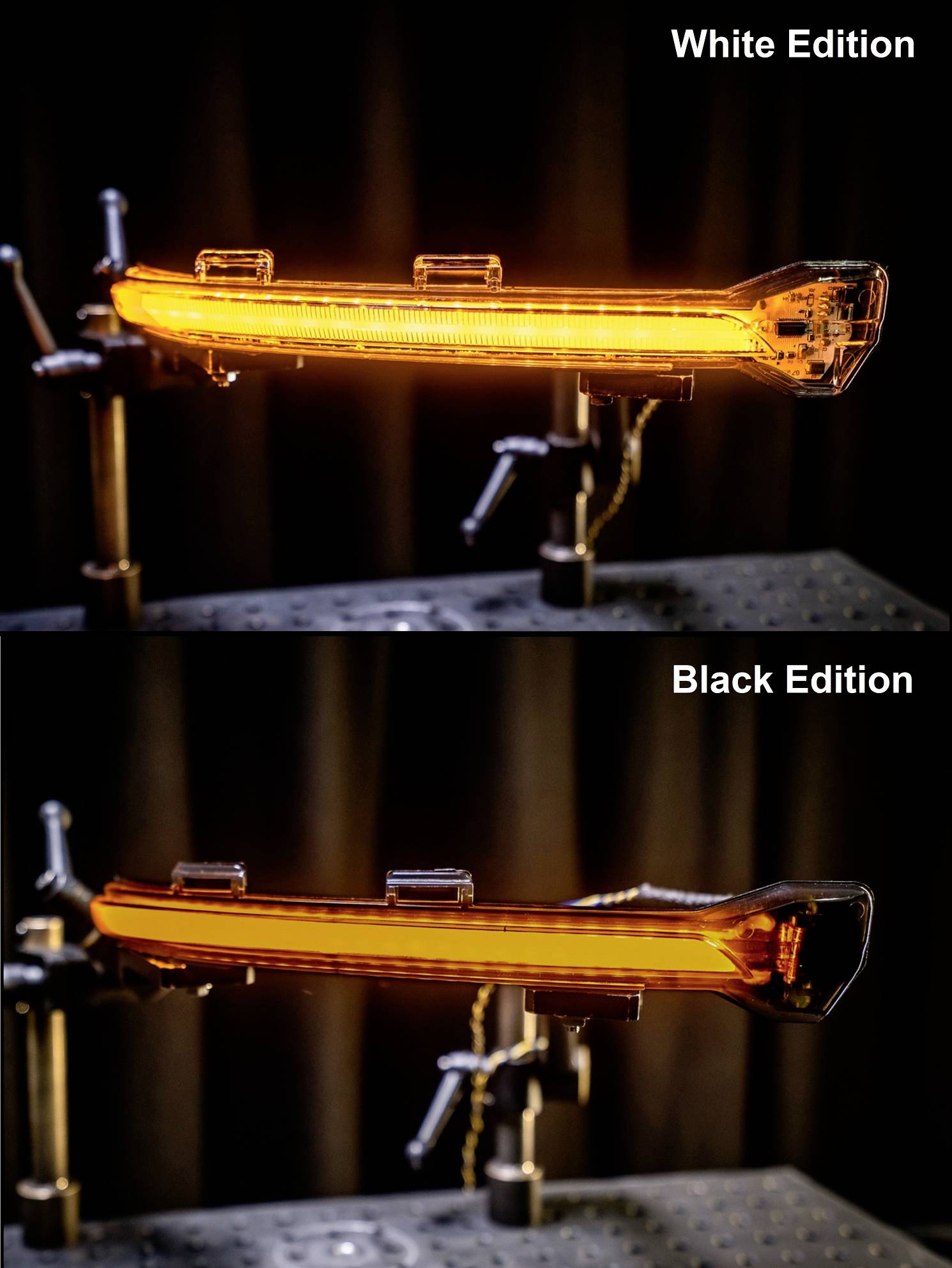 Due lampeggianti a confronto: quello superiore 'White Edition' mostra una luce arancione brillante, quello inferiore 'Black Edition' allo stesso modo. Entrambi montati su supporto.