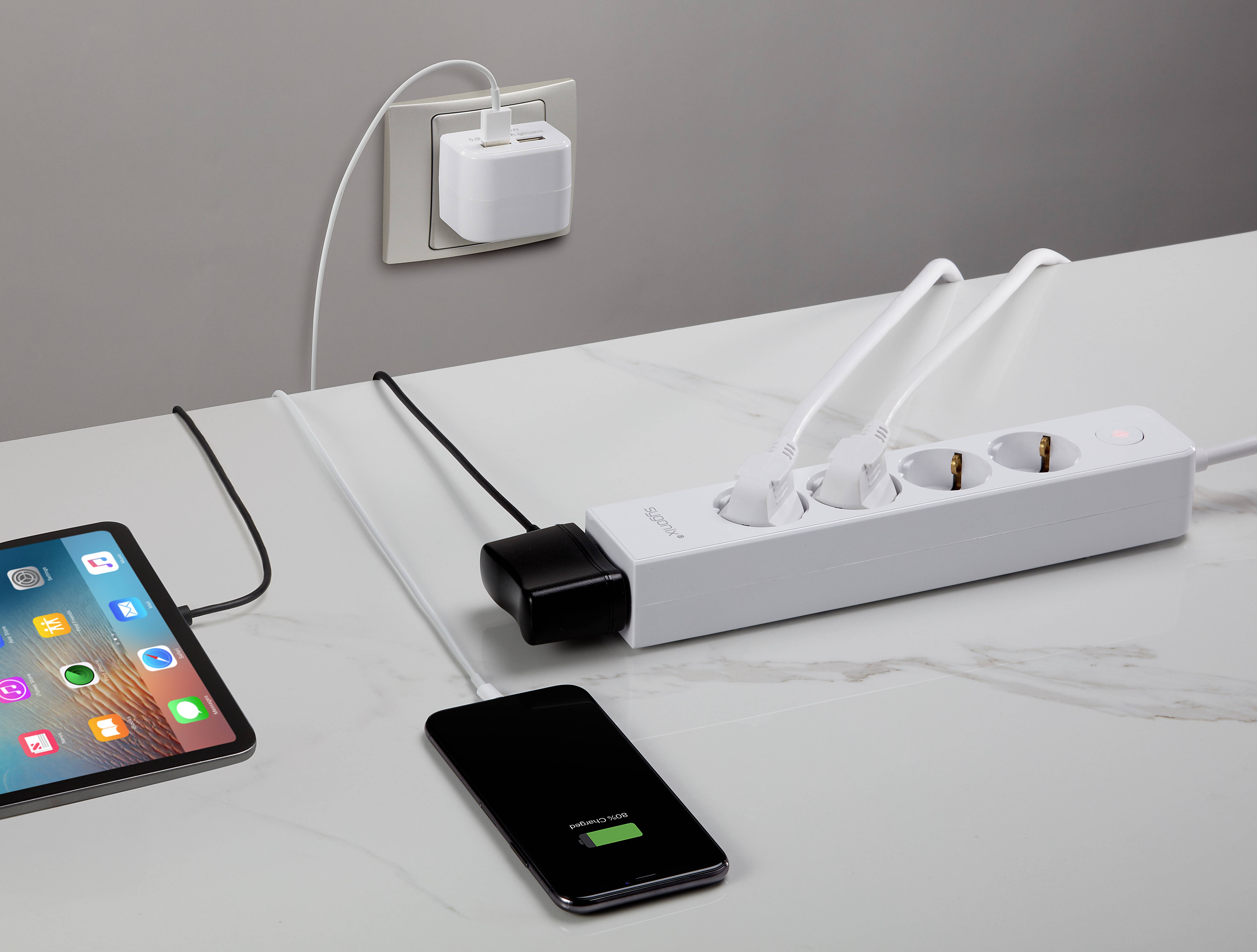 Un tablet e uno smartphone sono collegati a una presa multipla bianca appesa a una presa a muro.