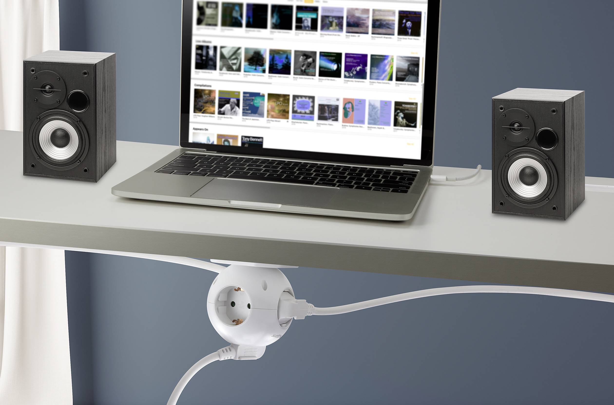 Un laptop su una scrivania mostra diversi copertine di musica o video sullo schermo. Accanto ci sono due altoparlanti.