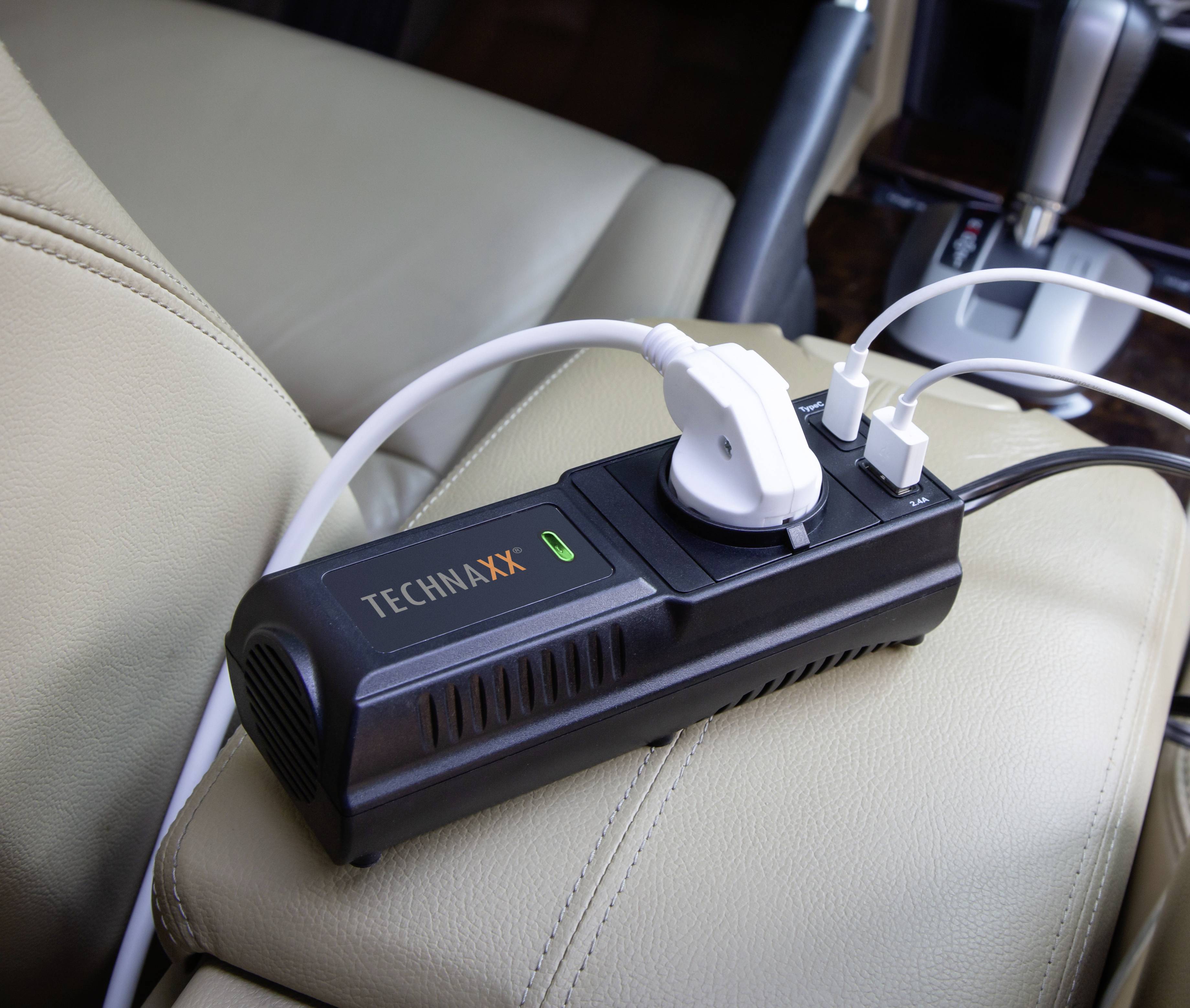 Adattatore di alimentazione con due porte USB e una presa elettrica, collegato all'interno di un'auto. Poggia su un sedile in pelle beige.