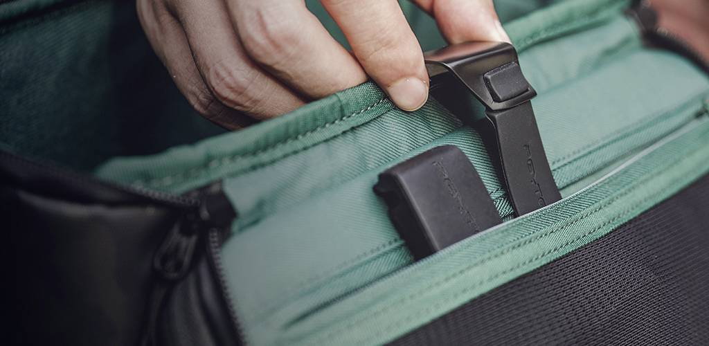 Una mano tira la zip nera di uno zaino verde per aprire un comparto.