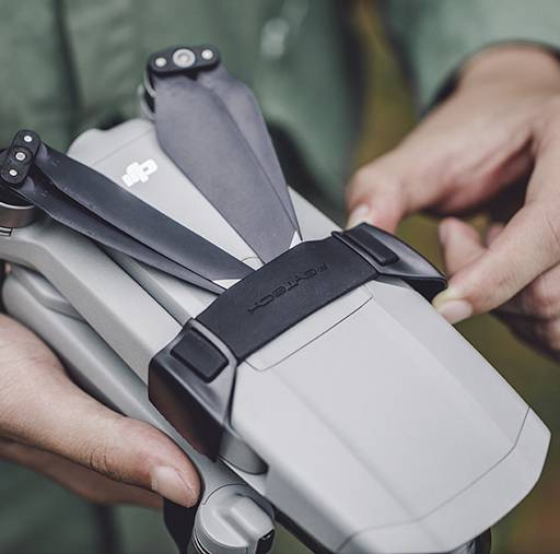 Una persona tiene un drone grigio con quattro eliche, pronto al decollo. Il focus è sul drone e sulle mani della persona.