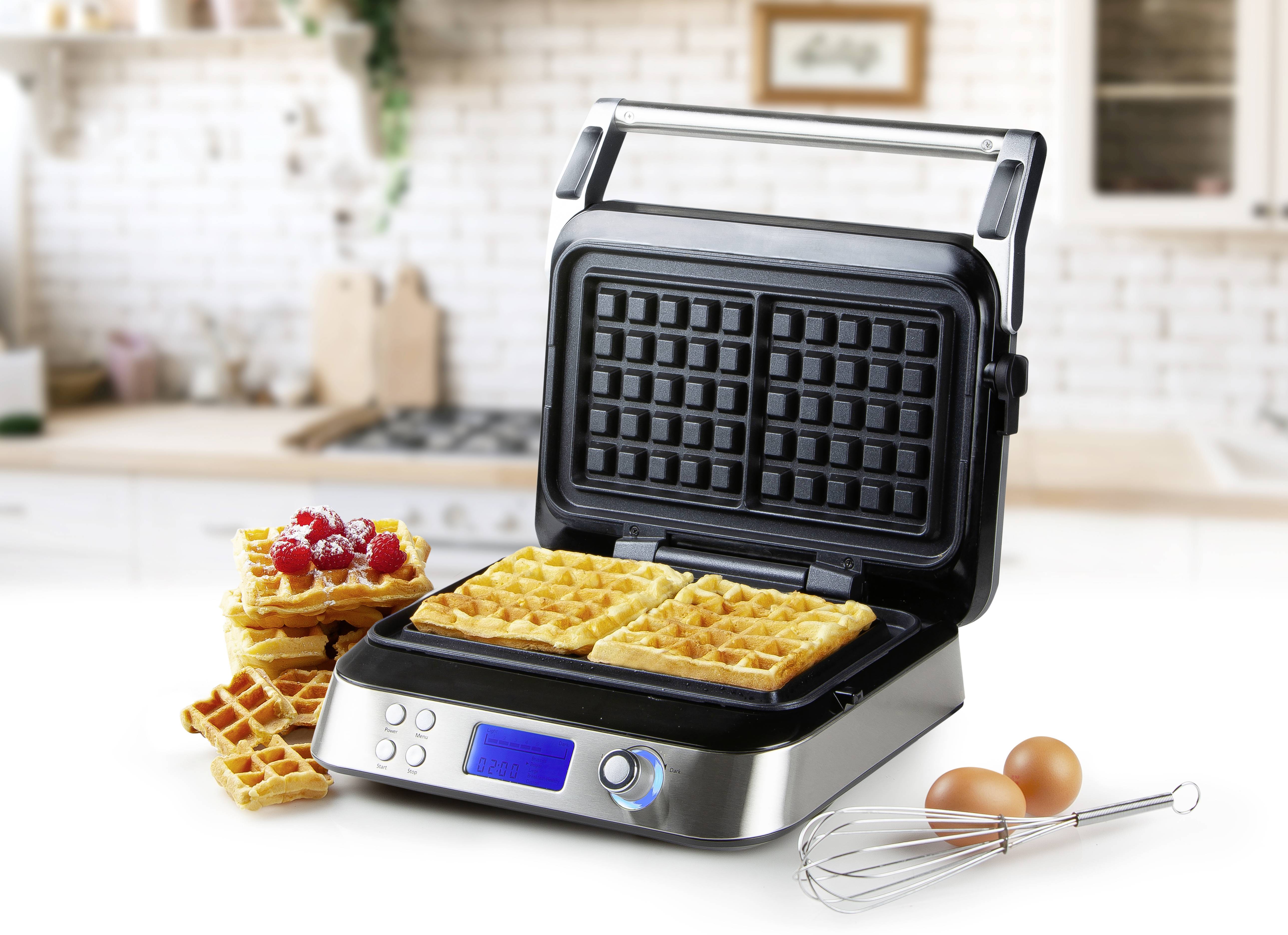Un moderno distributore automatico di cialde con il coperchio aperto e cialde pronte in una cucina. Accanto ci sono uova, una frusta e cialde.