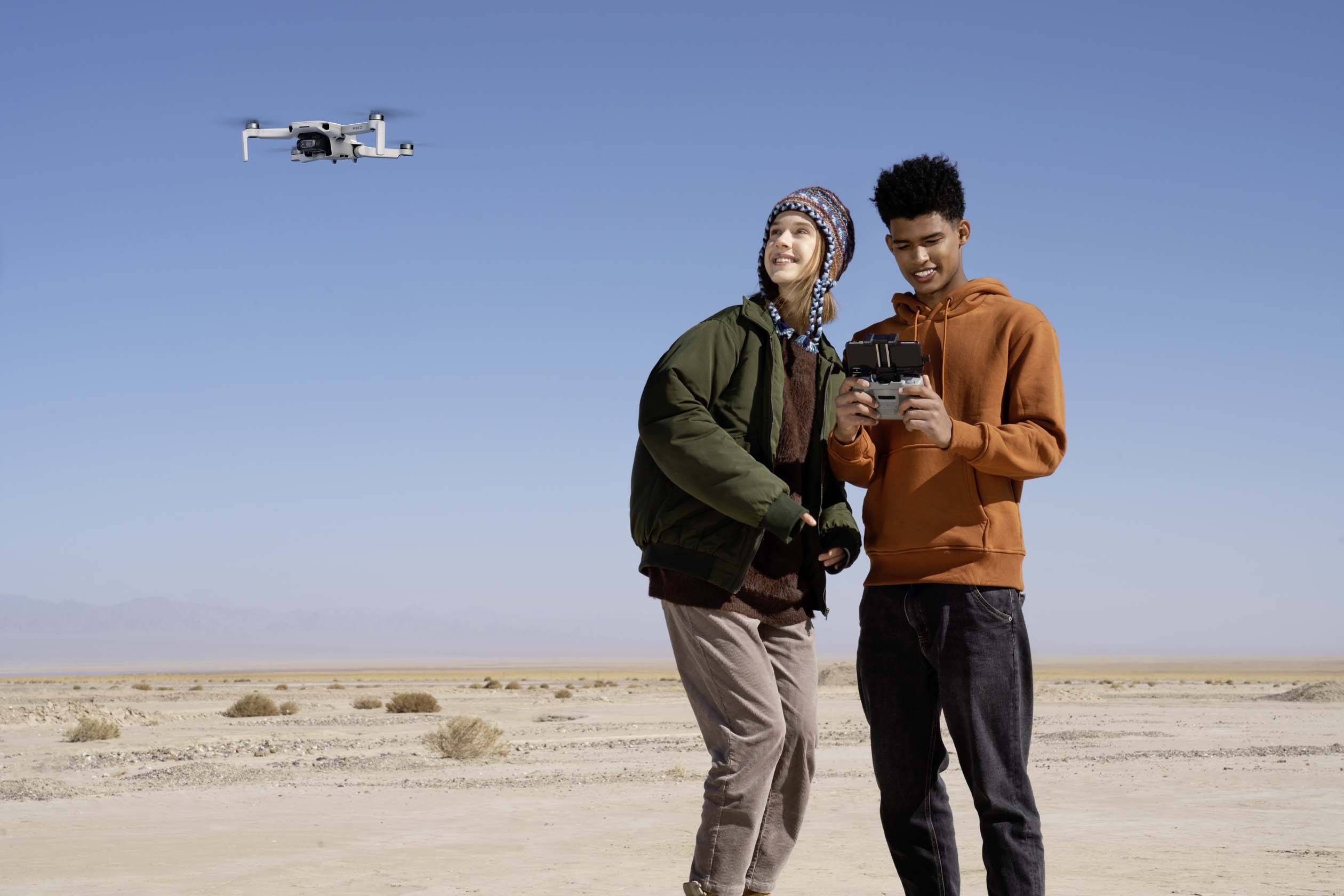 Due persone stanno in un deserto e controllano un drone in volo. Il cielo è chiaro e blu.