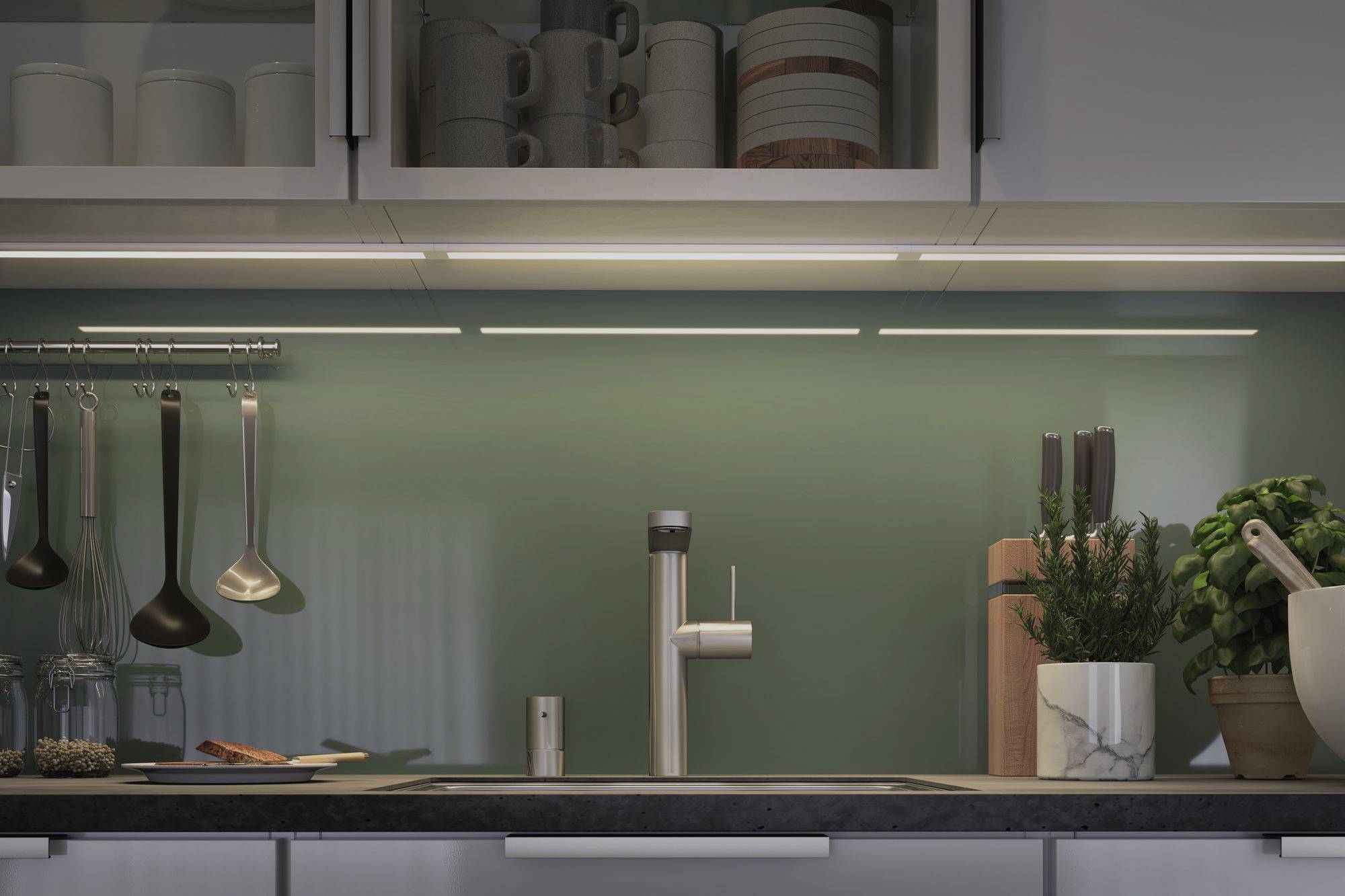 Cucina moderna con schienale in vetro verde, illuminazione LED, lavello in acciaio inox, spezie, piante e mensola sospesa con utensili da cucina.