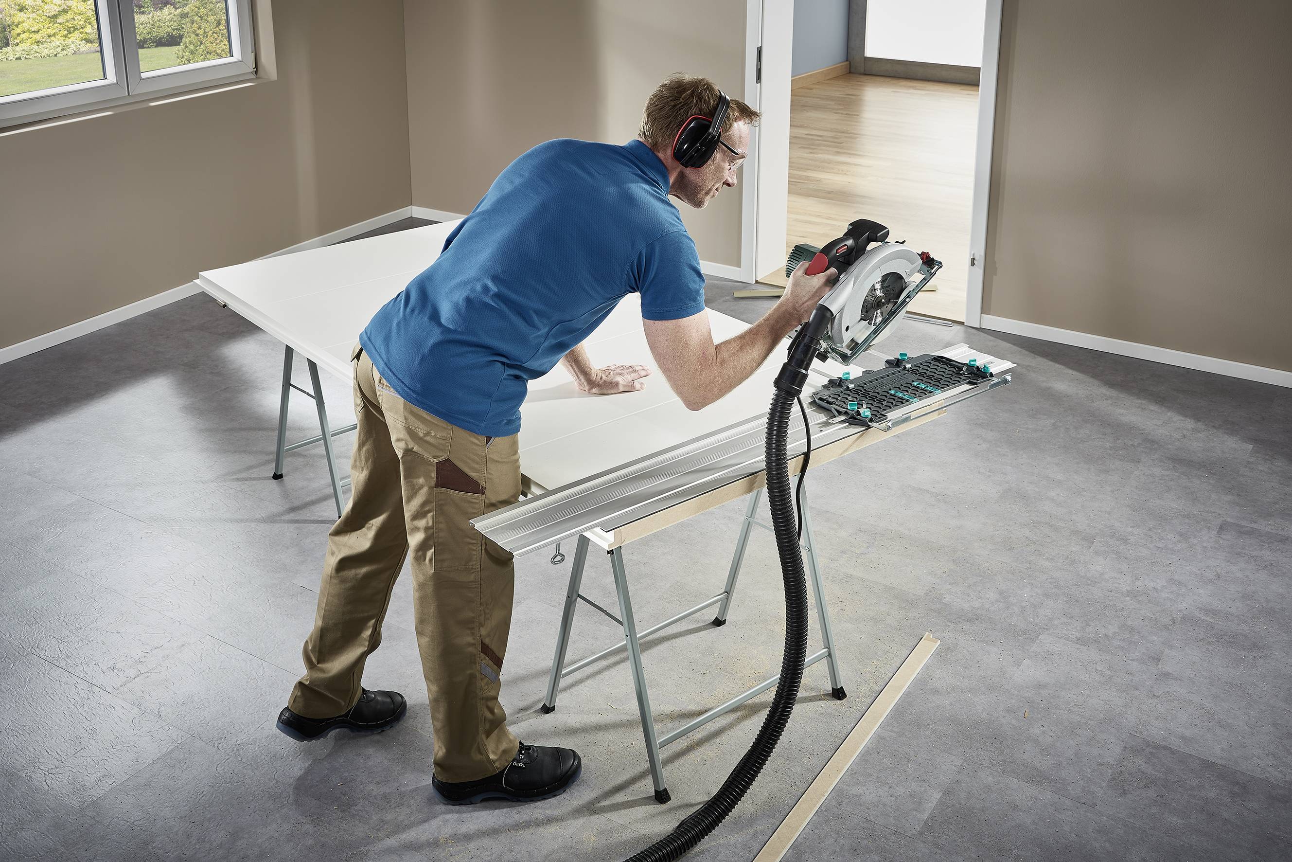 Una persona sta tagliando una grande tavola di legno con una sega circolare elettrica su un tavolo in una stanza luminosa.