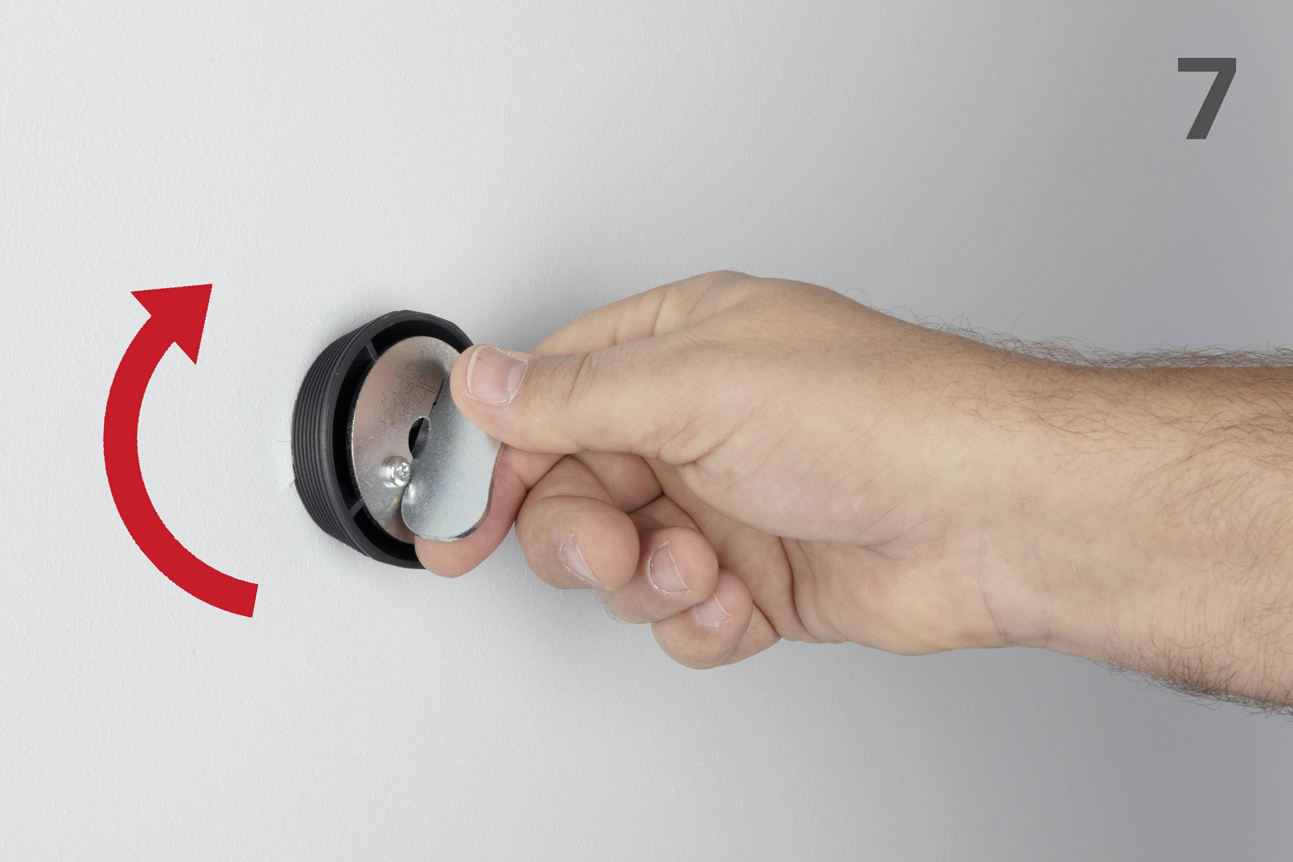 Una mano ruota un disco piatto sul muro in senso antiorario, una freccia rossa indica la direzione.