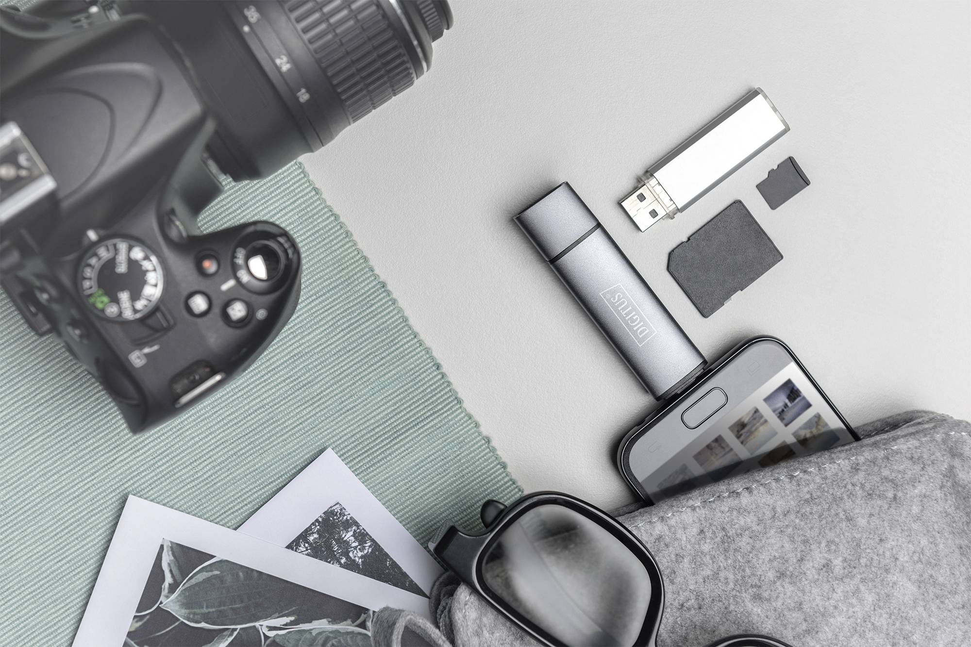 Macchina fotografica, chiavetta USB, smartphone, occhiali e foto su sfondo grigio; rappresenta la fotografia digitale e analogica.
