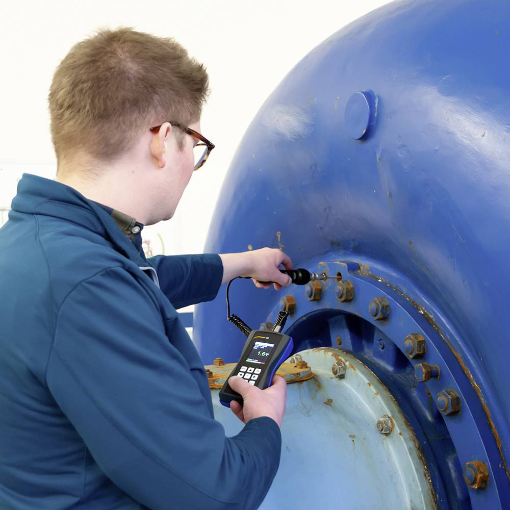 Una persona in abbigliamento da lavoro blu sta controllando lo stato tecnico di una grande macchina blu con un piccolo dispositivo.
