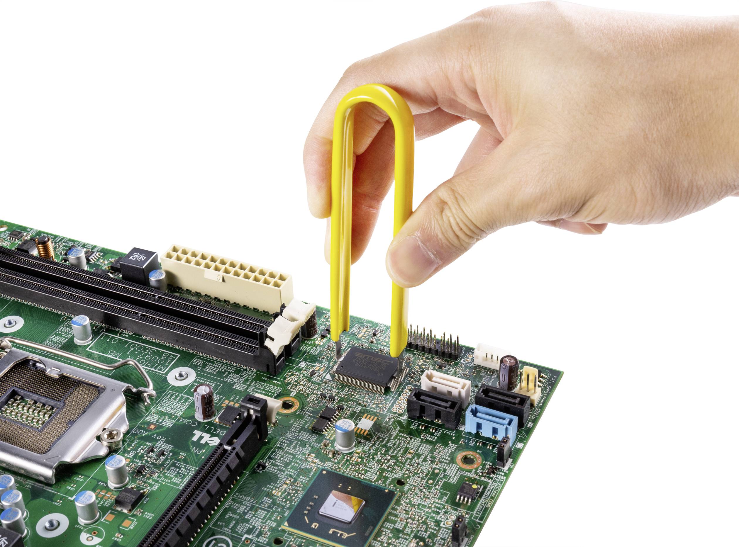 Una mano tiene un utensile giallo e rimuove un chip da una scheda elettronica verde con vari componenti elettronici.