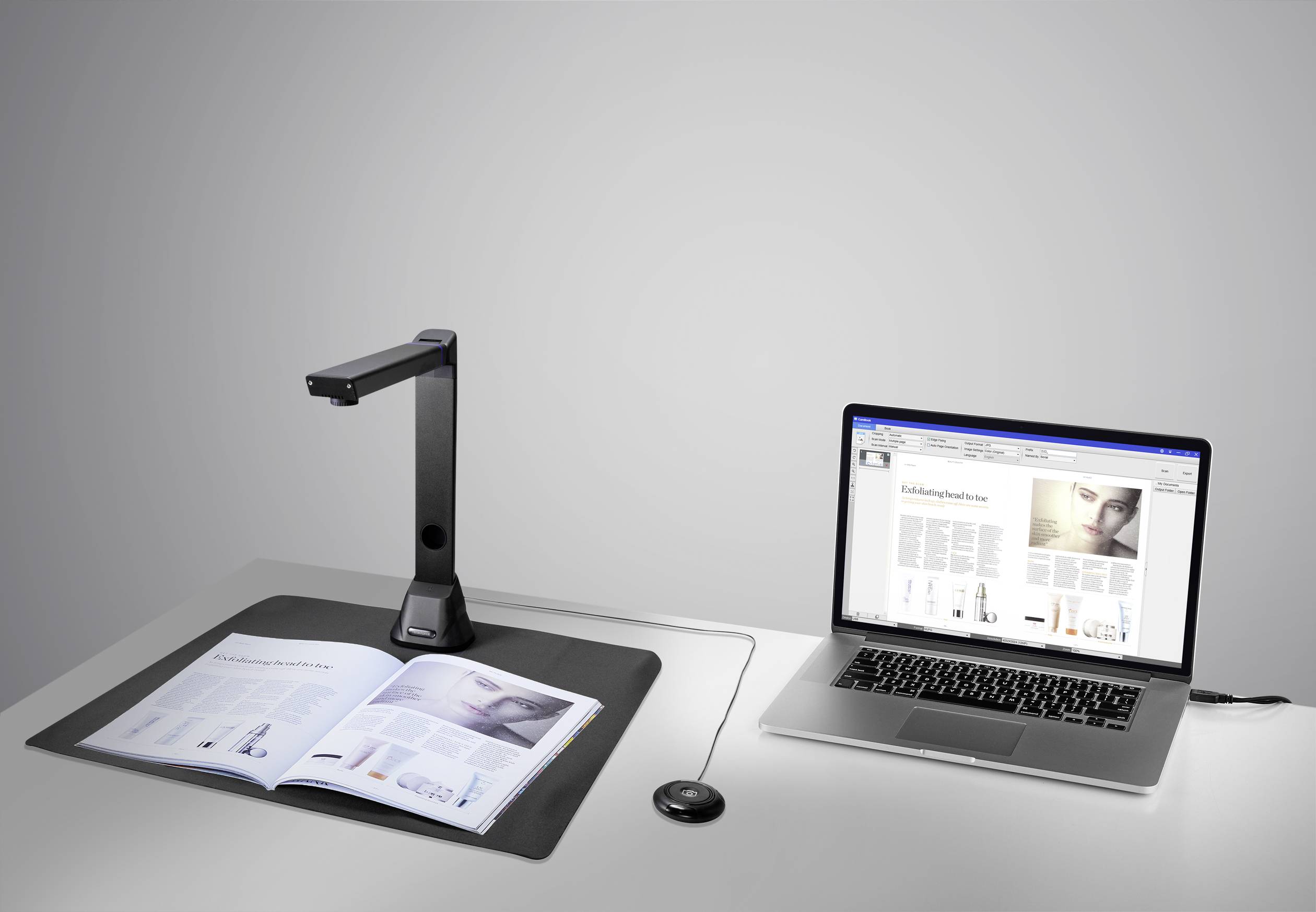 Uno scanner per documenti sta acquisendo un libro aperto. Accanto a esso un laptop, il cui schermo mostra il contenuto del libro scansionato.