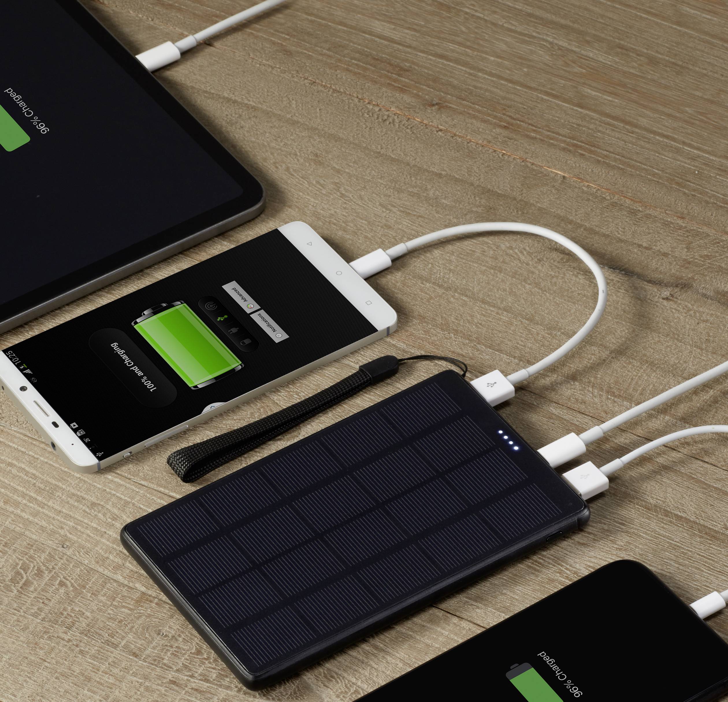 Tablet e smartphone vengono caricati su un tavolo di legno con un caricabatterie solare portatile. Tutti i dispositivi mostrano l'indicatore di carica.