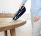 Una persona aspira le briciole da un tavolo di legno con un aspirapolvere portatile in una stanza luminosa con pavimento in legno.