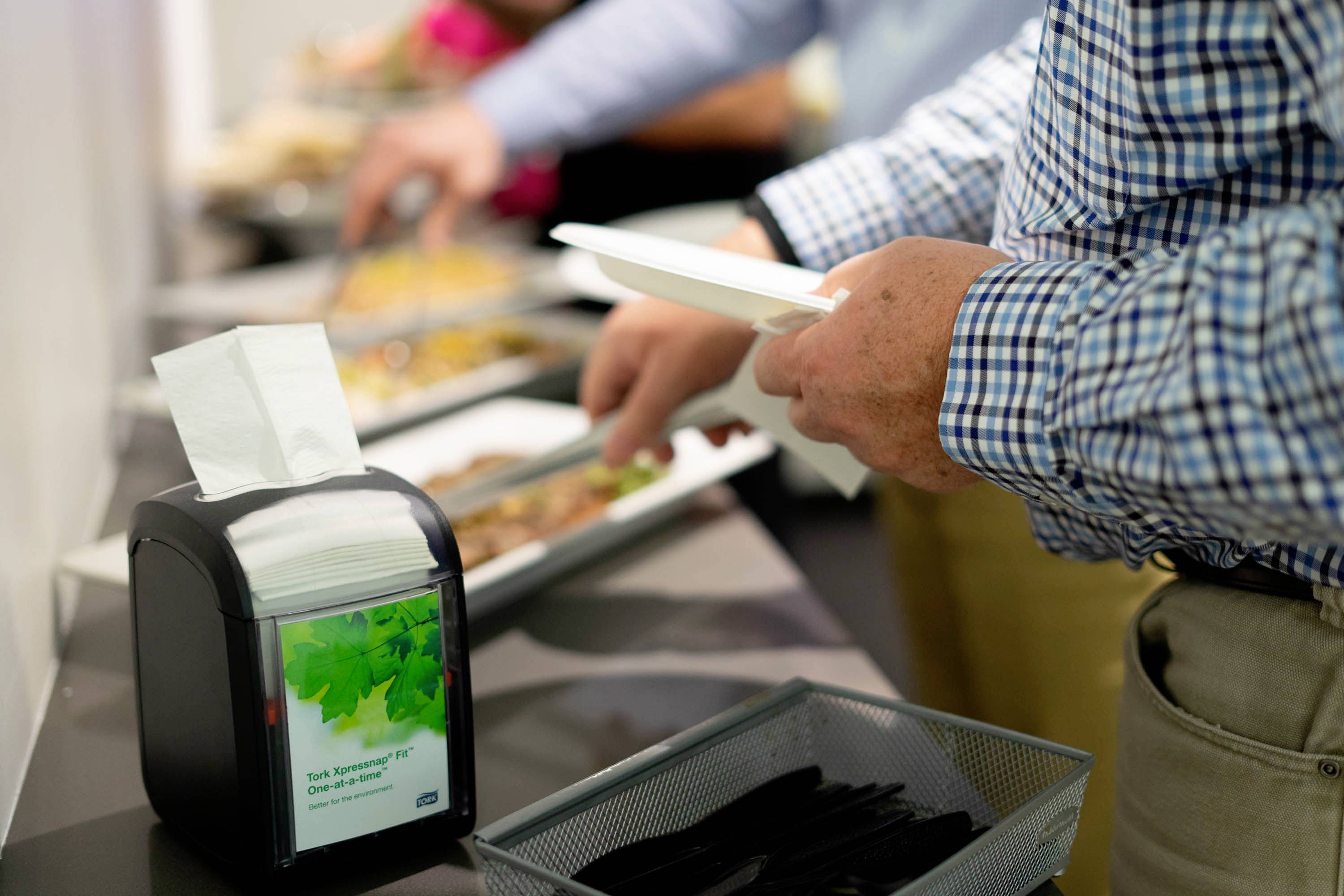 Una persona preleva del cibo da un buffet in una mensa. In primo piano c'è un porta tovaglioli.