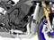 Primo piano del motore e della ruota anteriore di una moto, che mostra il blocco motore, un ammortizzatore dorato e la ruota blu.