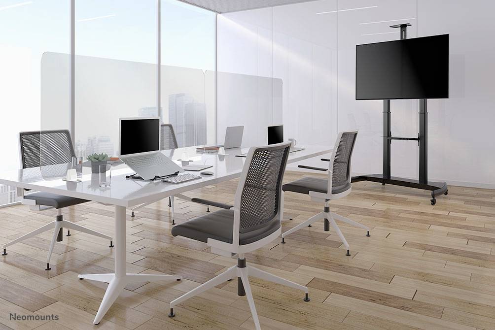 Sala riunioni moderna e luminosa con tavolo bianco, quattro sedie da ufficio, laptop, blocco notes e schermo piatto su supporto. Vista dalla finestra sulla città.