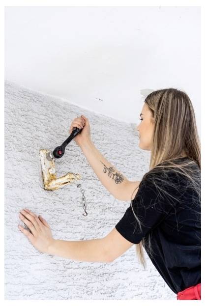 Donna che usa una chiave a cricchetto per stringere o allentare una staffa metallica montata a parete su una parete bianca con texture.