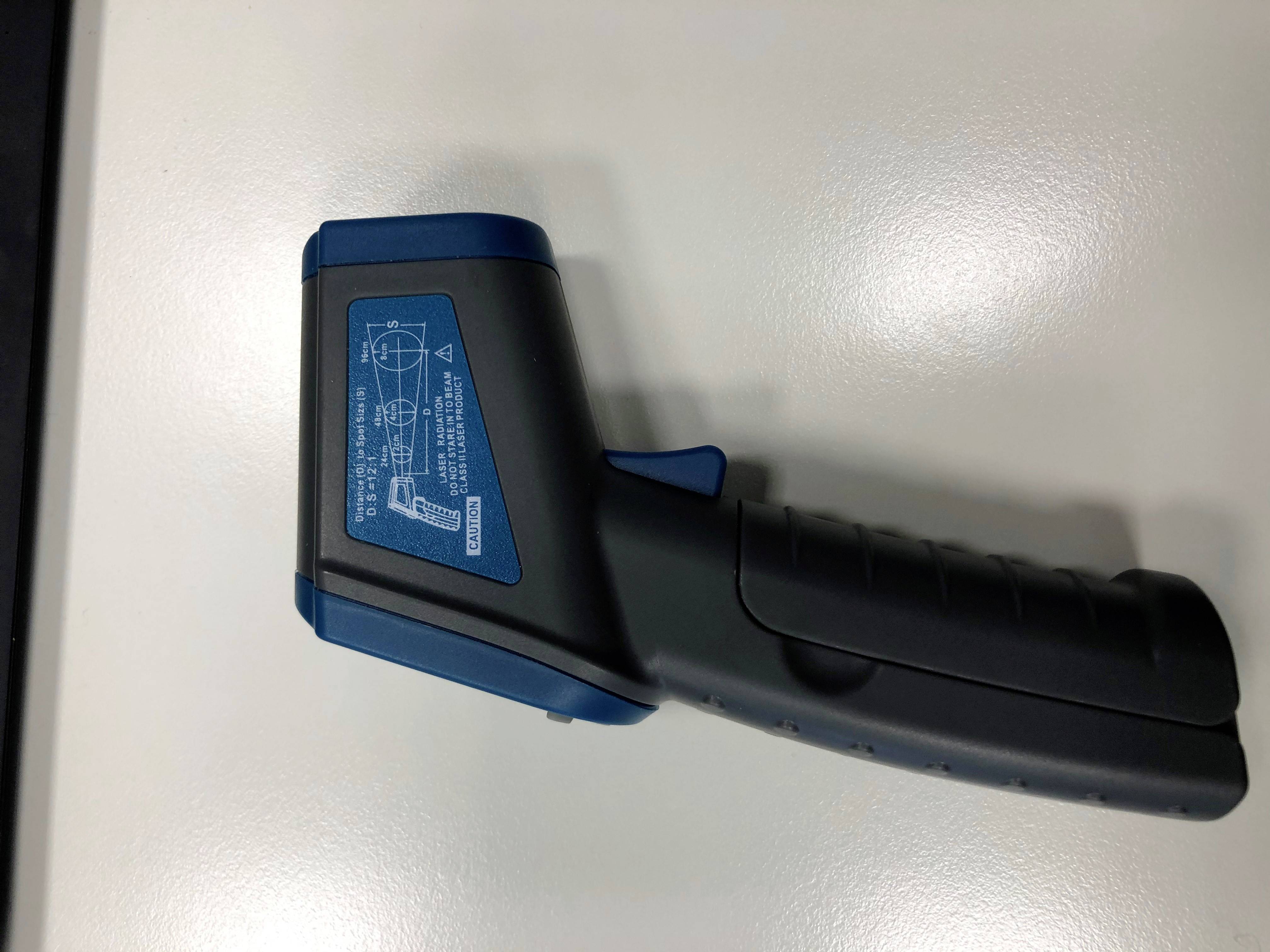 Un misuratore di temperatura a infrarossi con custodia blu e nera su una superficie bianca. Ha un'etichetta con istruzioni.