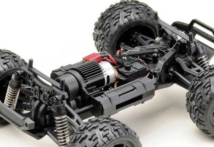 Primo piano di un'auto radiocomandata che mostra la sospensione, il motore e i collegamenti dei cavi. L'immagine evidenzia la struttura tecnica e i dettagli meccanici.