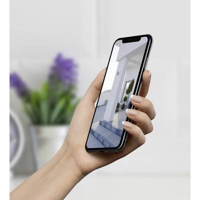Una persona tiene in mano uno smartphone che mostra un'immagine di architettura moderna sullo schermo. Sullo sfondo si intravede una decorazione di stanza sfocata.