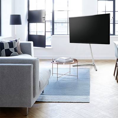 Un soggiorno moderno con un divano grigio, un tavolo rotondo in vetro su un tappeto blu e un grande televisore a schermo piatto.