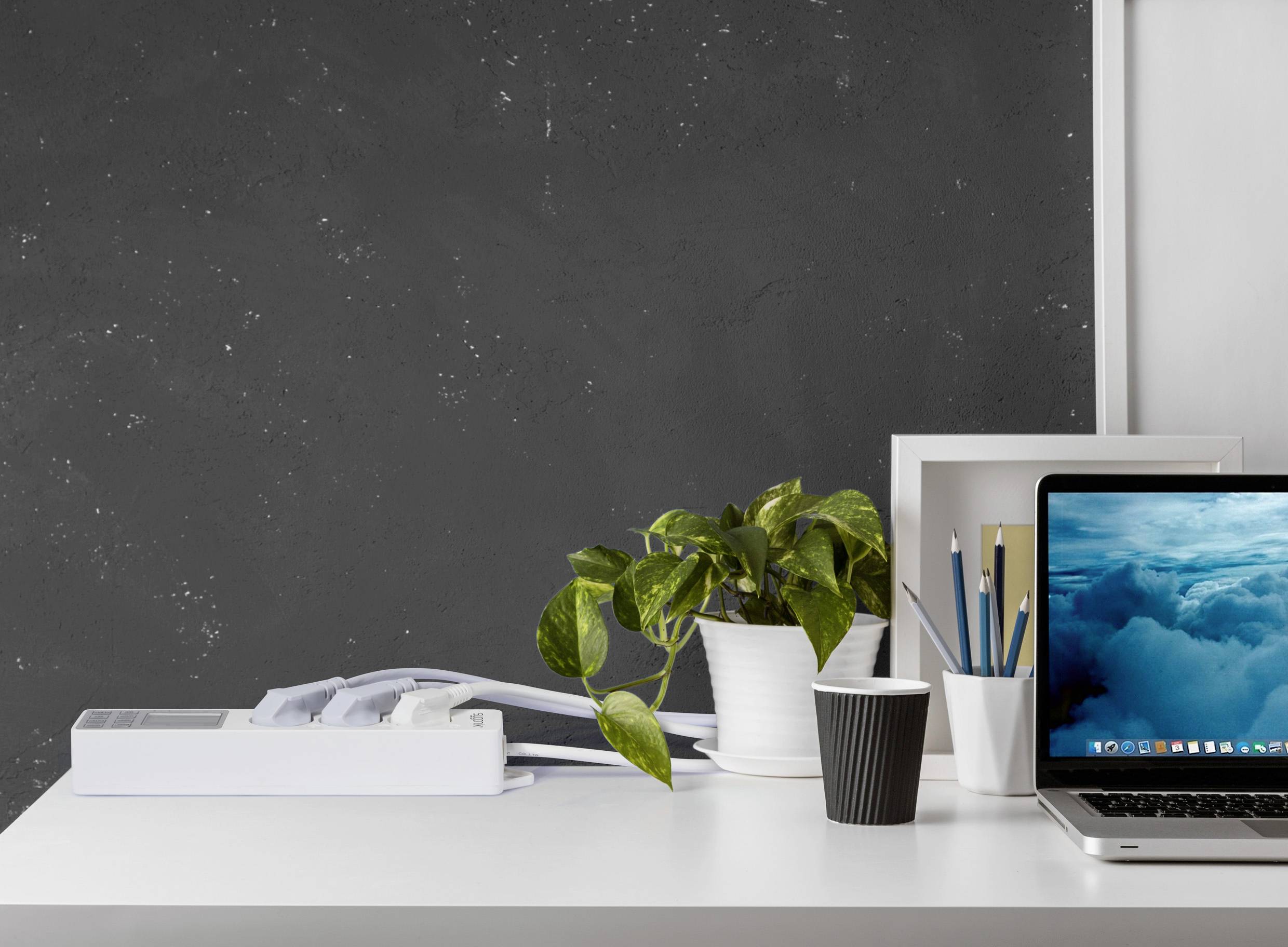 Postazione di lavoro moderna con laptop, piante e penne davanti a una lavagna scura. Un mucchio di fogli e una tazza di caffè nero sono anch'essi visibili.