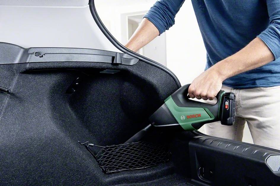 Una persona sta usando un aspirapolvere portatile per pulire il bagagliaio di un'auto. L'aspirapolvere è compatto e senza fili.