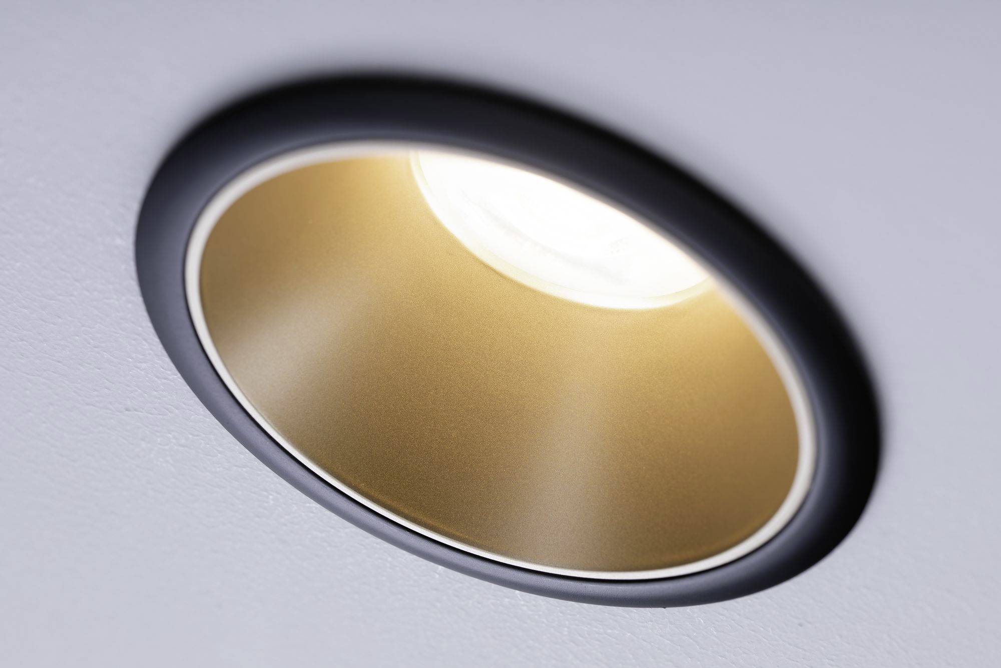 Un'applique rotonda da soffitto con riflettore color oro emana una luce calda.