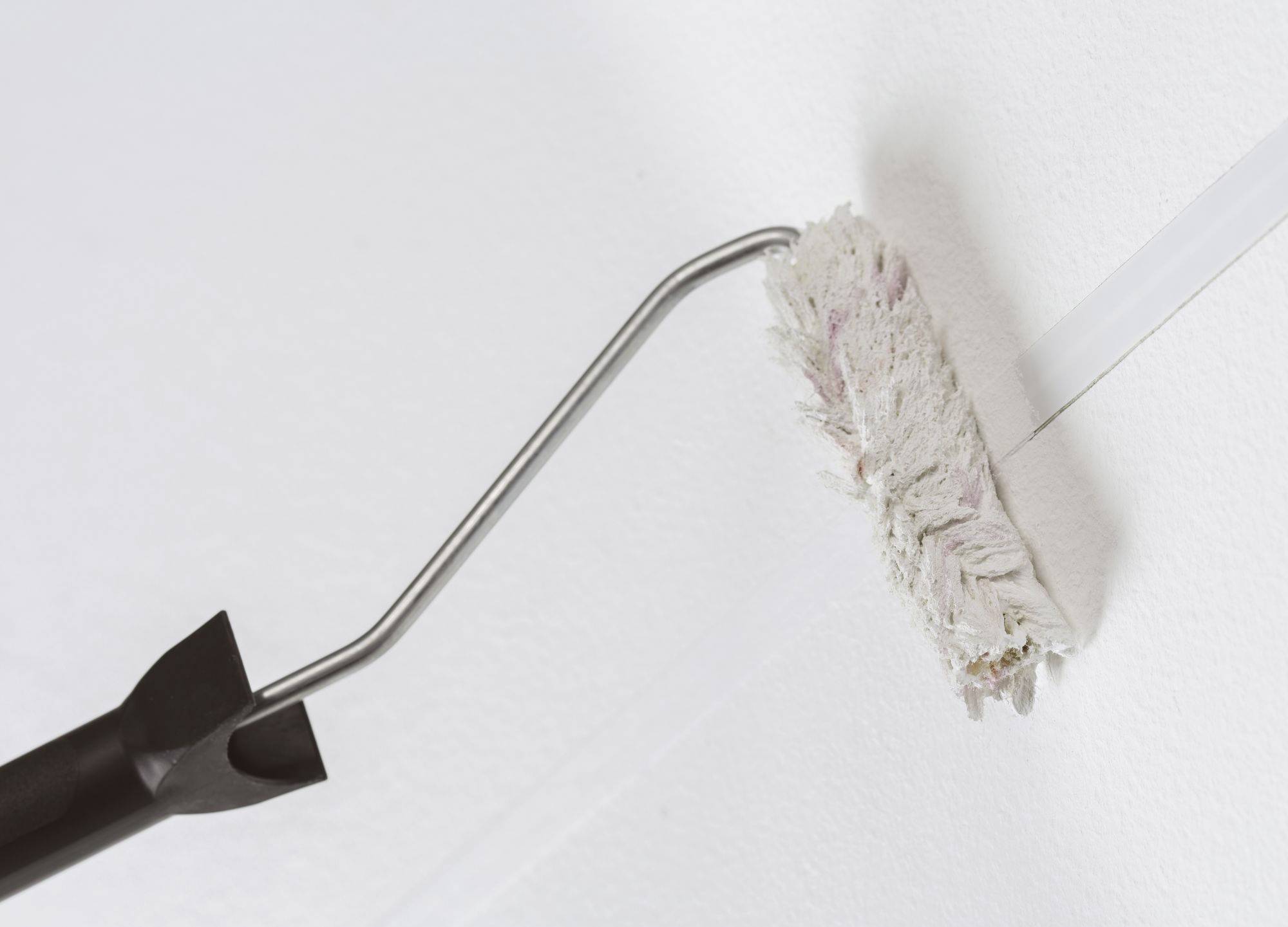 Un rullo da pittura con manico viene utilizzato per applicare vernice bianca su una parete. Il rullo rimane vicino a un bordo diritto.